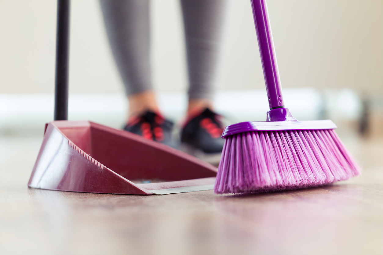 Young woman cleaning her flat with broom and collector at home.