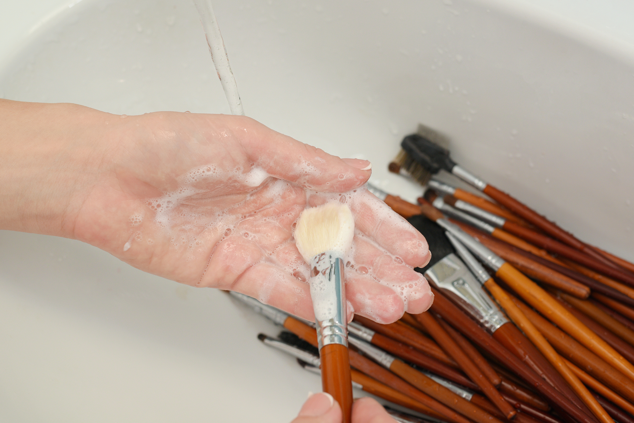 woman is washing dirty makeup brush with soap and foam in the sink