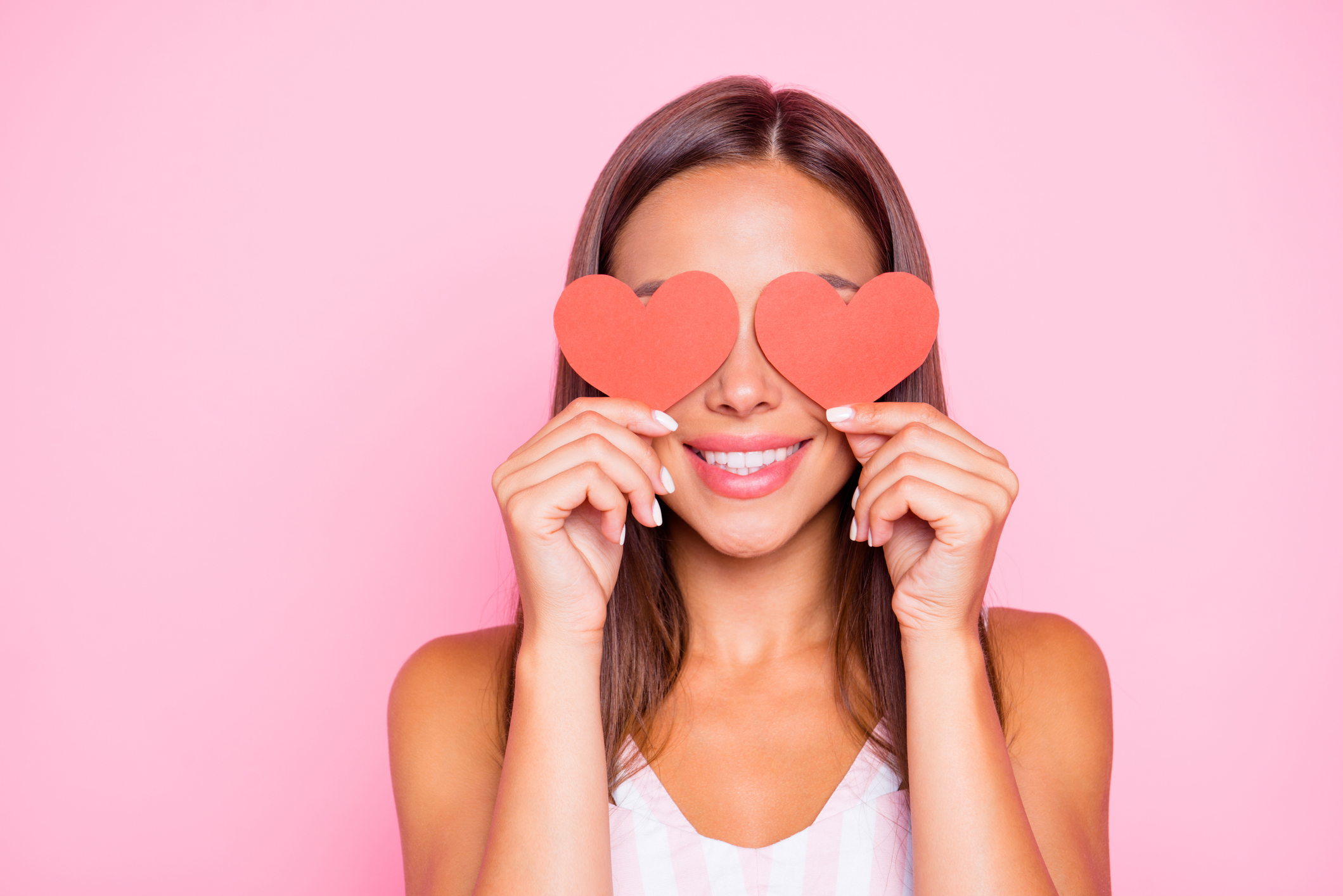 Close up portrait of cute sweet pretty beautiful lovely gorgeous hold two small little thematic red shape cards close eyes she isolated on vivid pink pastel background in her white casual wear