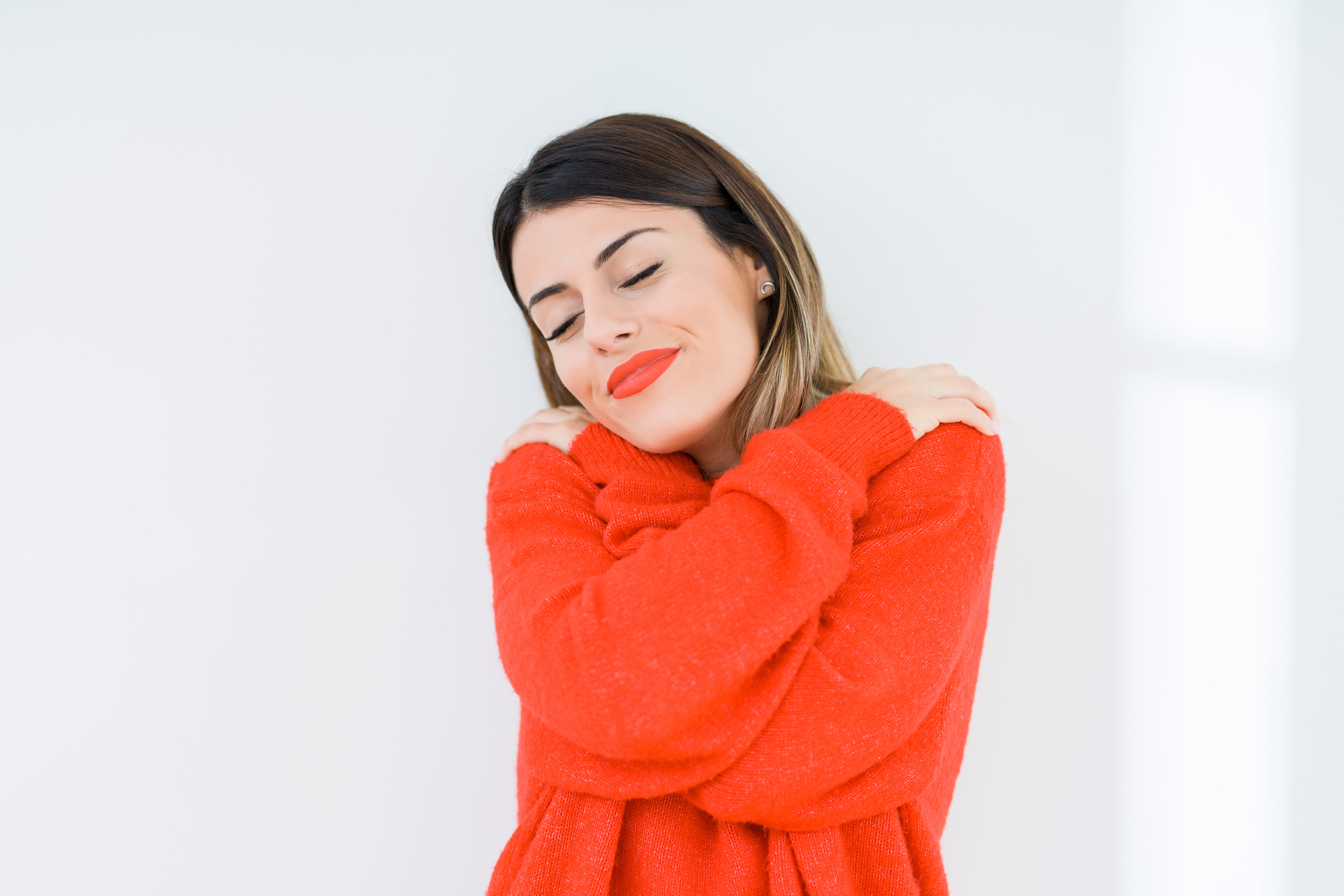 Young woman wearing casual red sweater over isolated background Hugging oneself happy and positive, smiling confident. Self love and self care