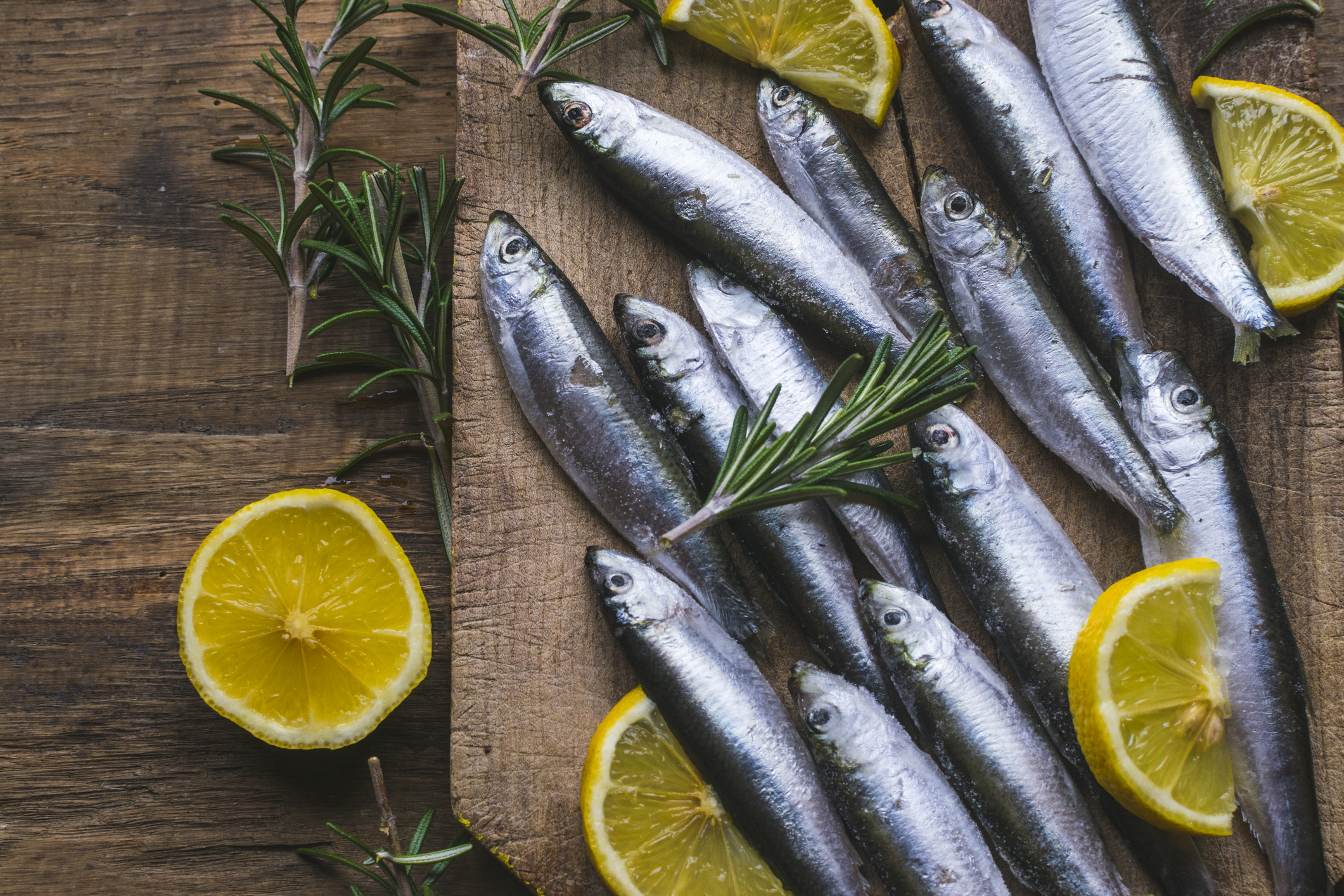 Fresh frozen sardines with lemon and rosemary on old, dark, wooden table