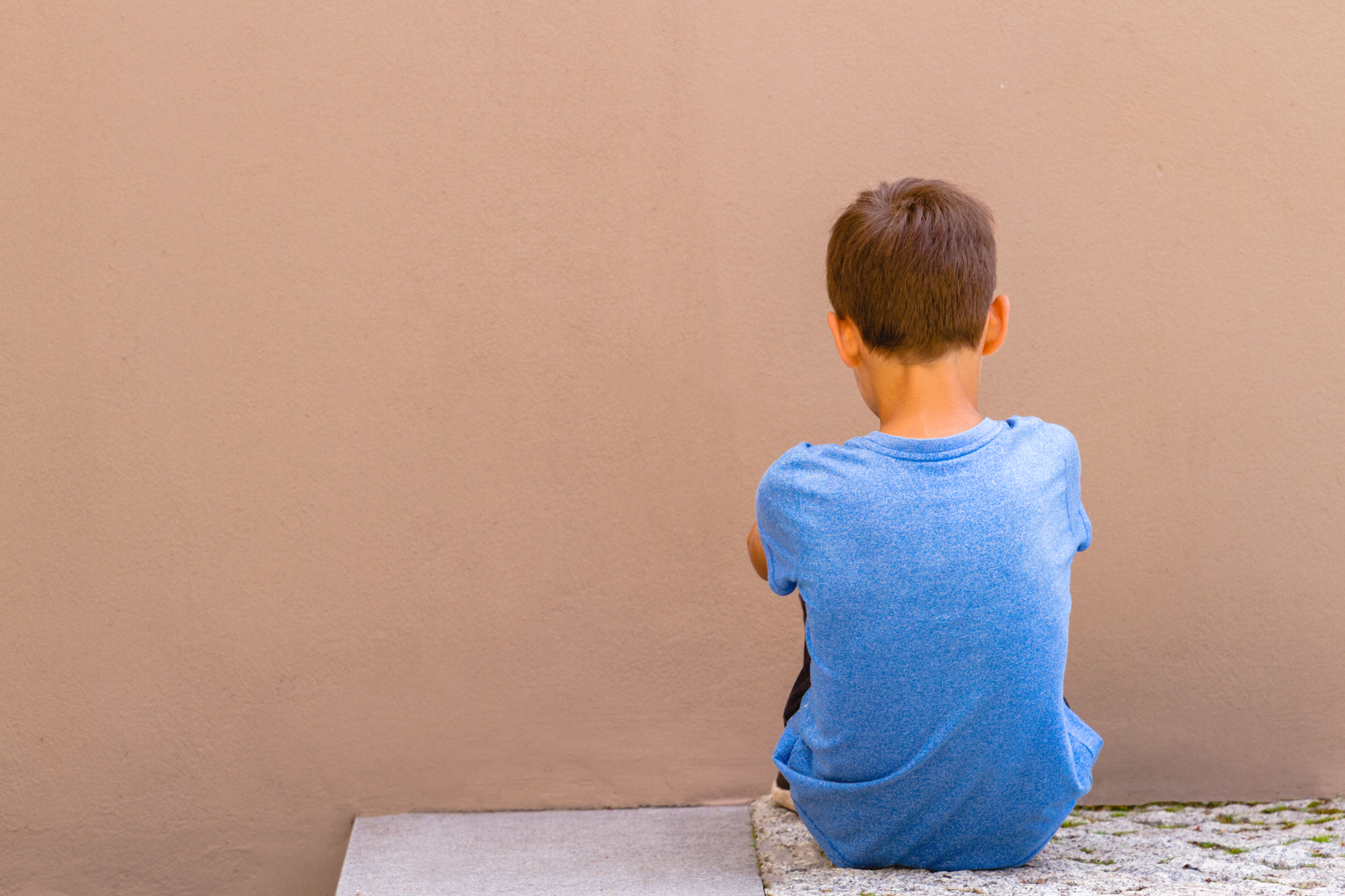 Sad alone boy sitting on the ground behind the wall outdoor