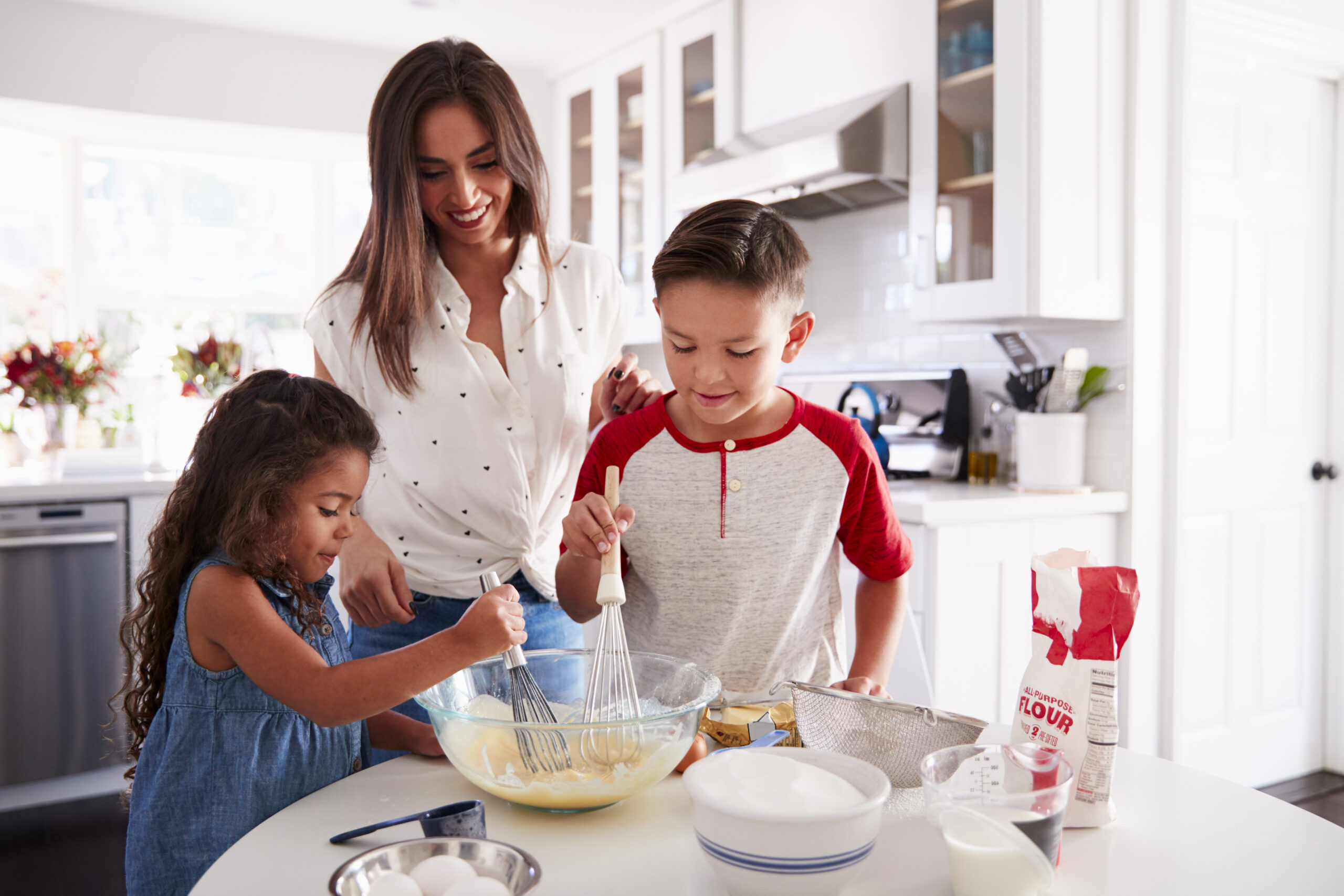 Brother and sister making cake mixture together at the kitchen table with their mum, waist up