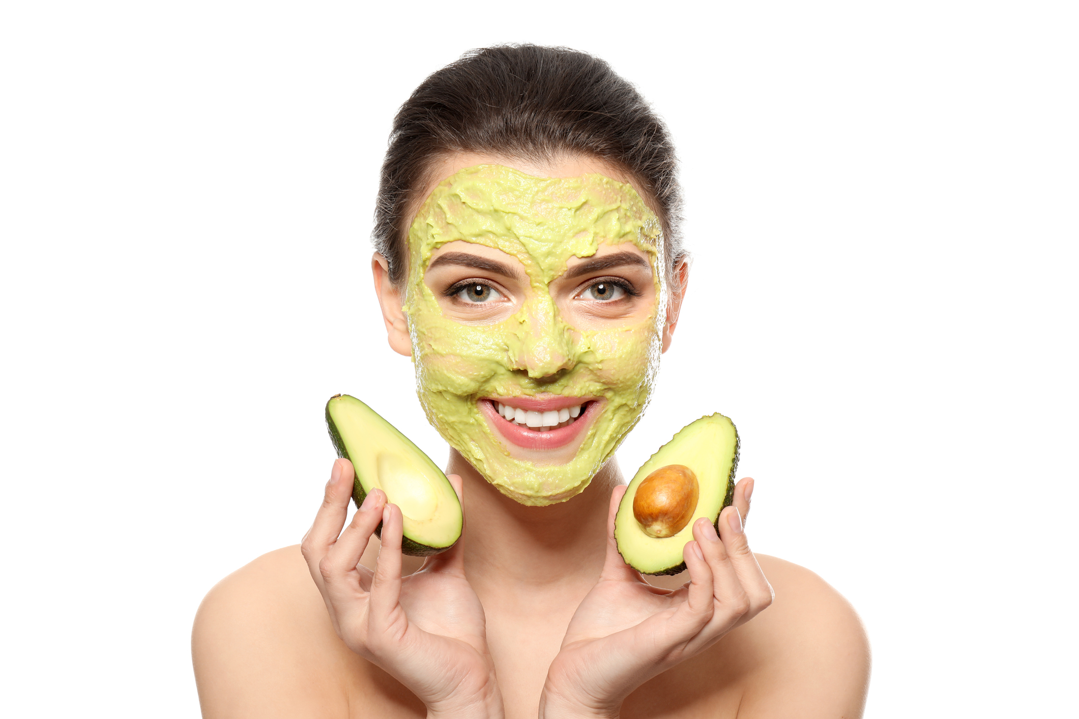 Beautiful young woman with facial mask and fresh avocado on white background