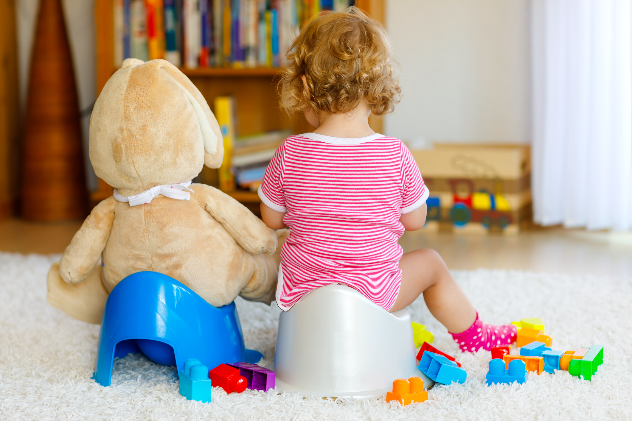 Closeup of cute little 12 months old toddler baby girl child sitting on potty. Kid playing with big plush soft toy. Toilet training concept. Baby learning, development steps