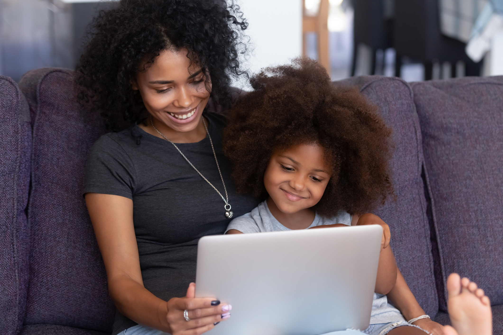 Smiling african mother and kid daughter having fun with computer