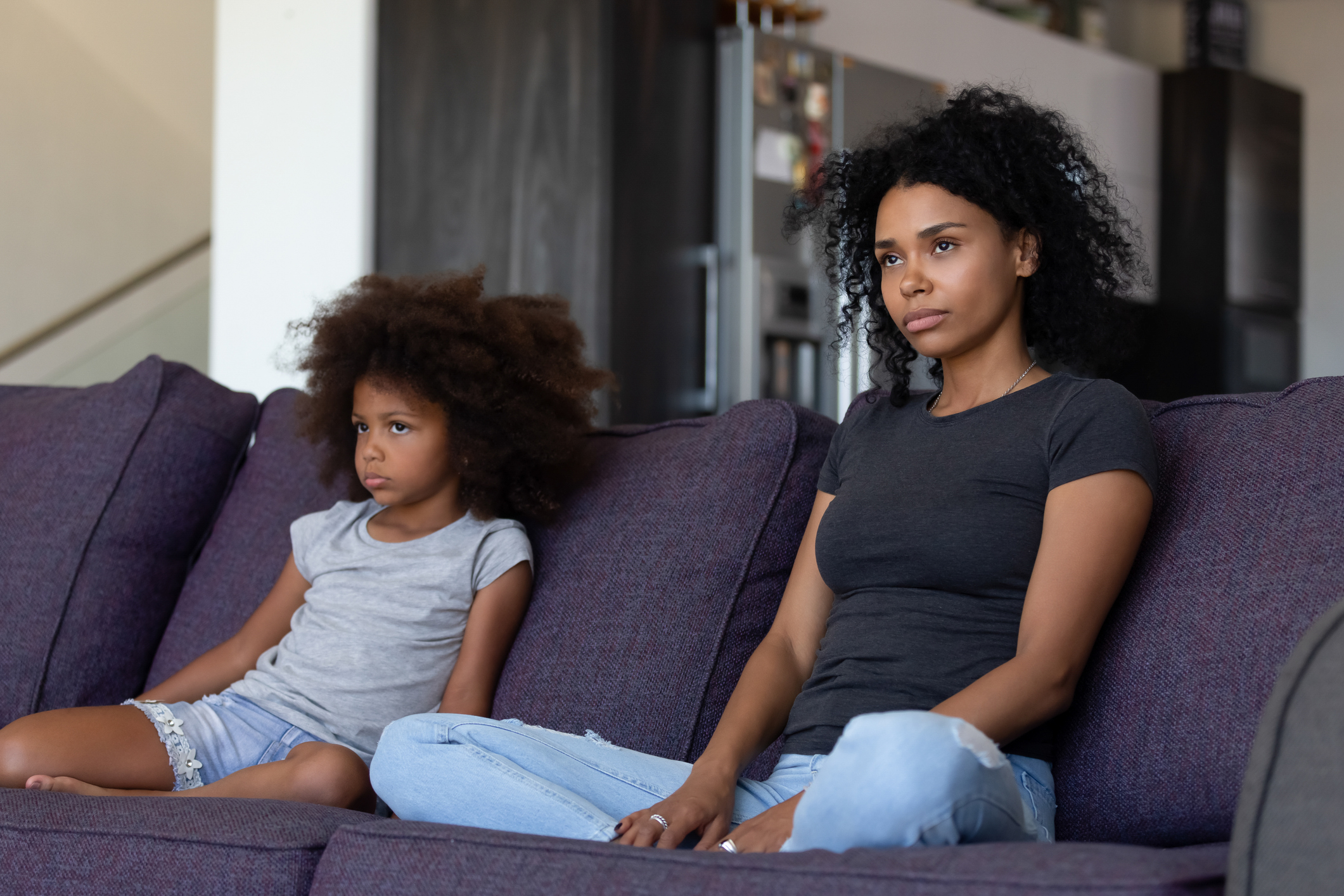 Sulky african child and mother sitting on sofa not talking