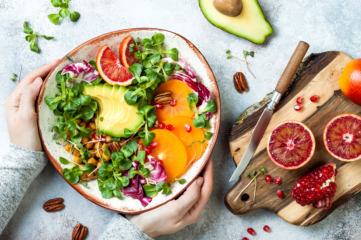 Vegan, detox Buddha bowl with turmeric roasted  chickpeas, greens, avocado, persimmon, blood orange, nuts and pomegranate. Top view, flat lay