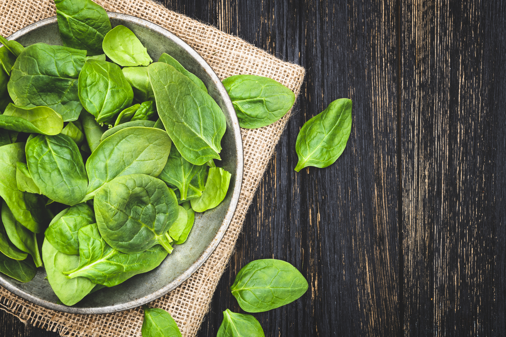 Fresh spinach leaves in bowl on rustic wooden table