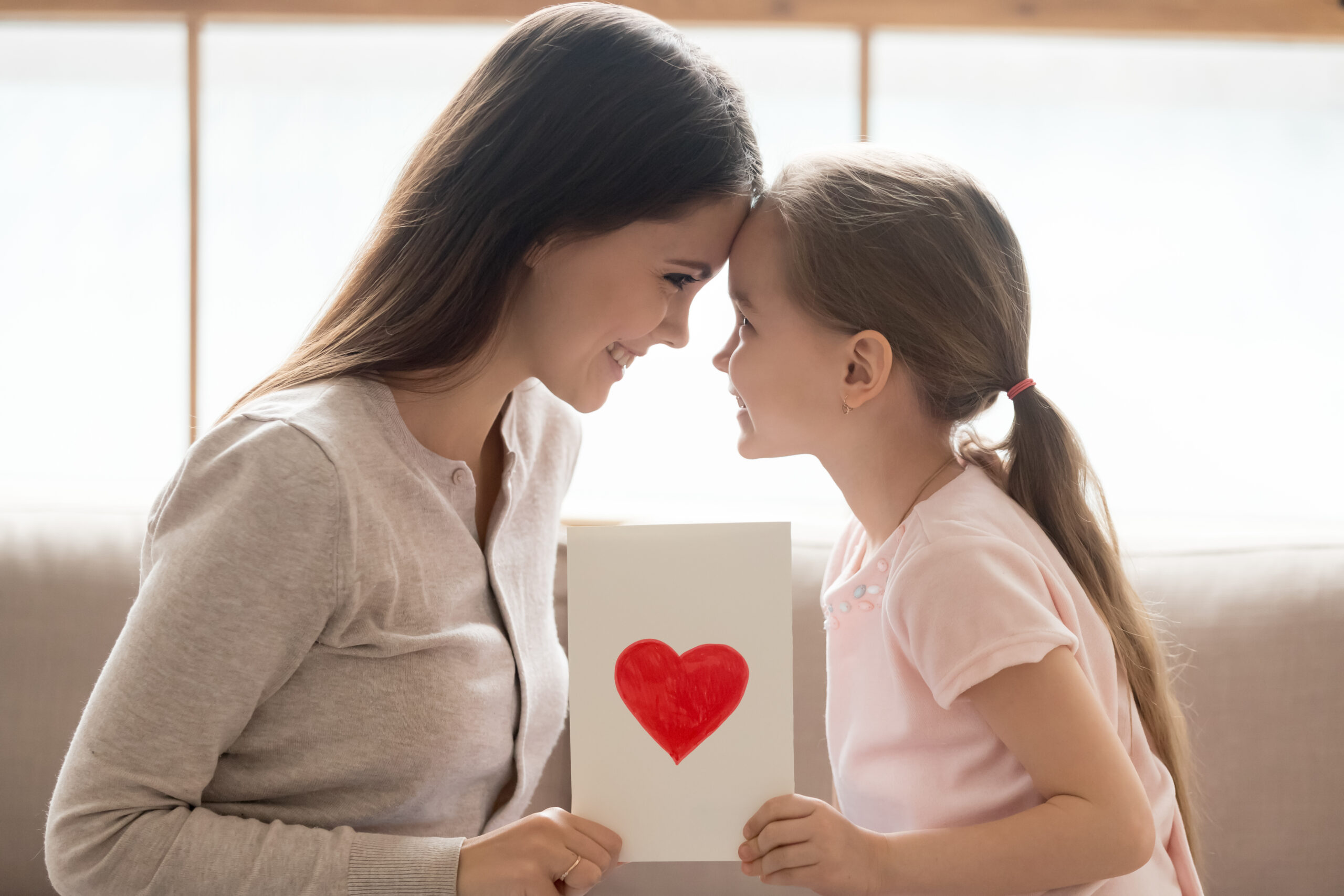 Happy mom and kid daughter holding greeting card with heart