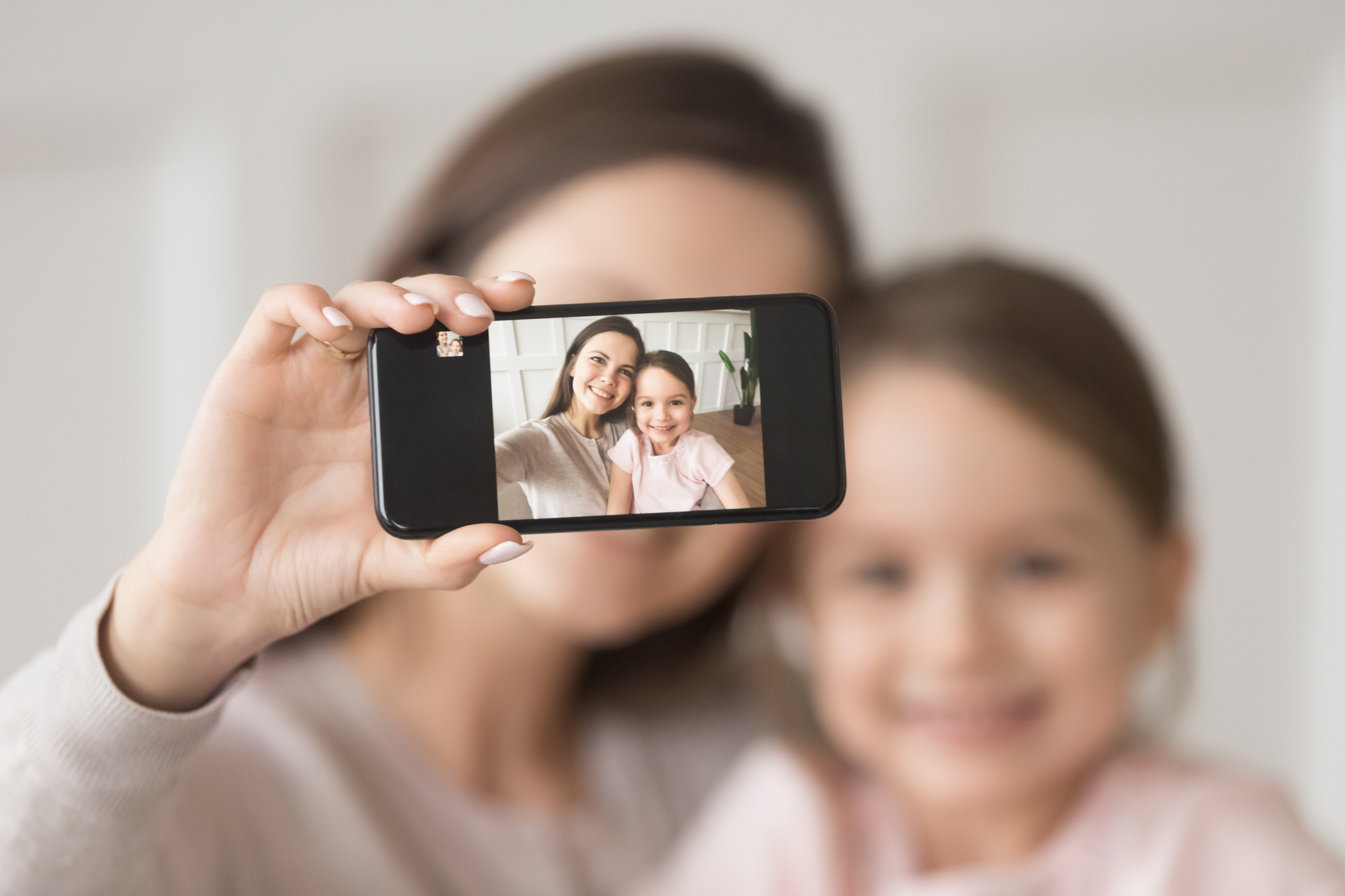 Happy mother holding phone taking selfie on cellphone with daughter