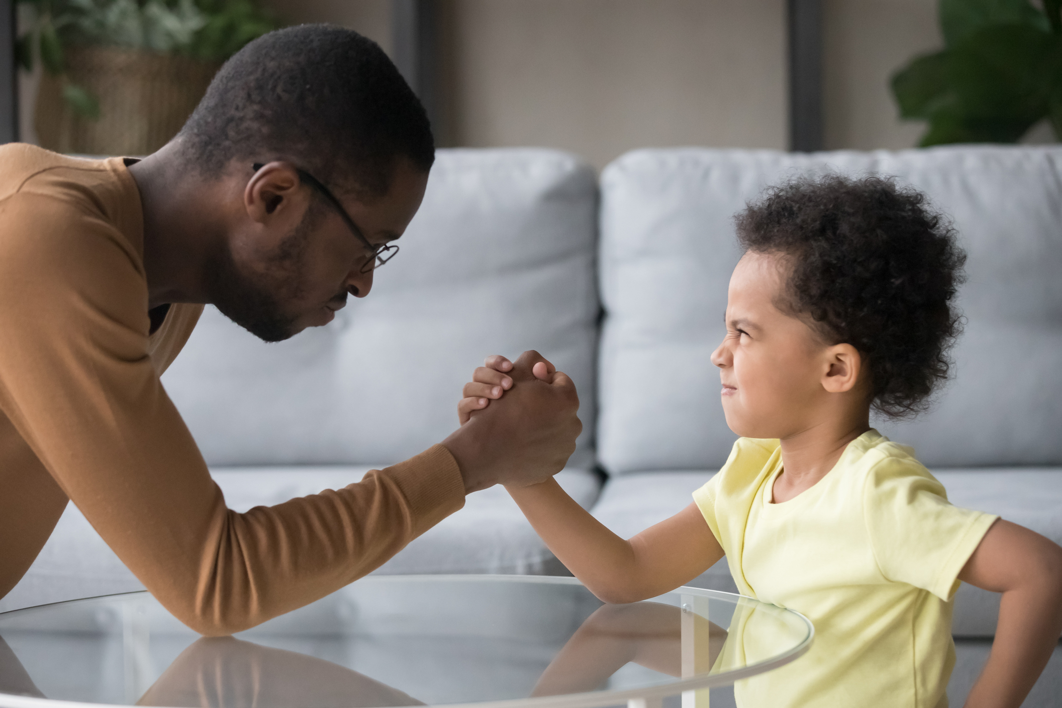 African dad and kid son with funny angry faces armwrestling