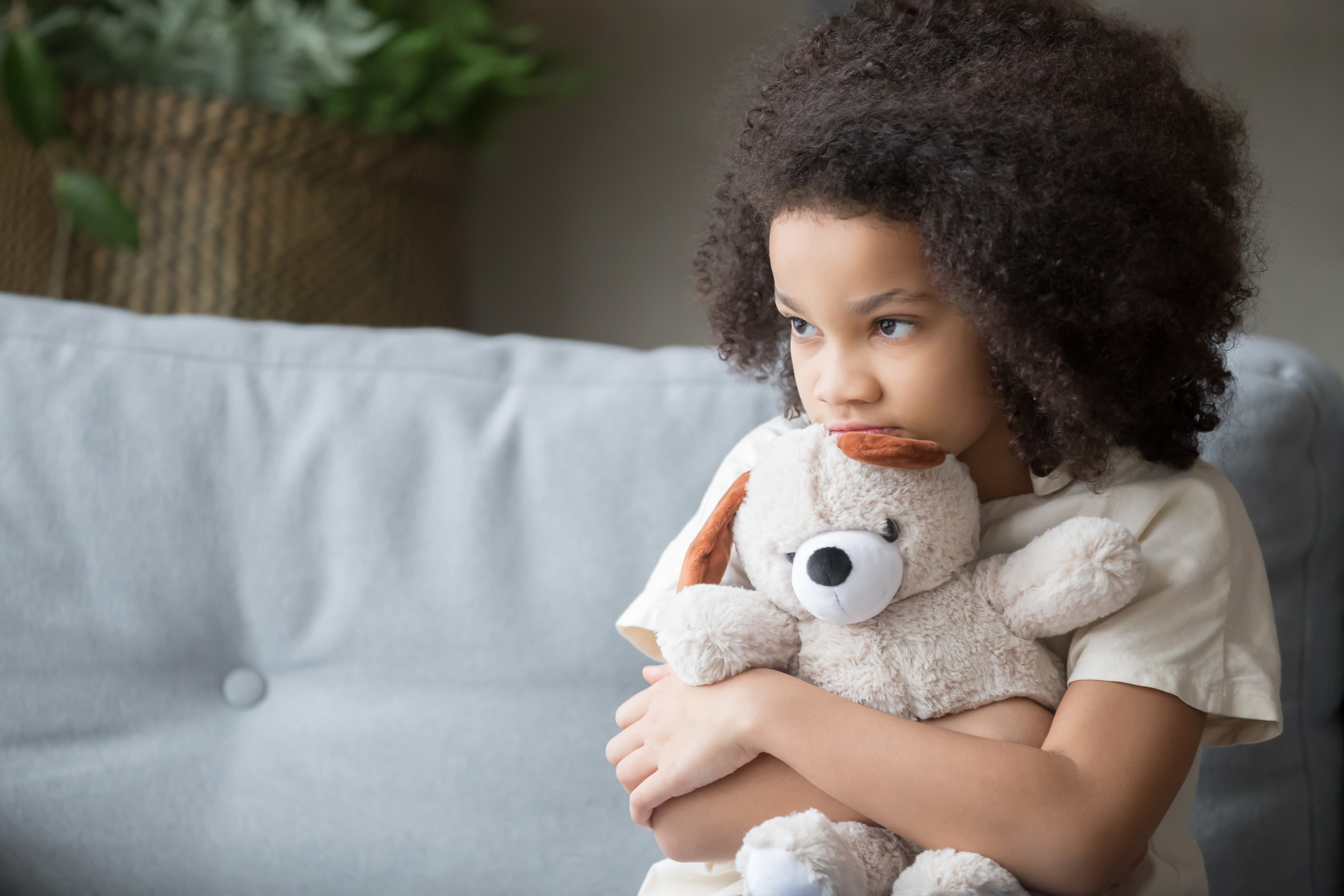 Upset lonely african kid girl holding teddy bear looking away