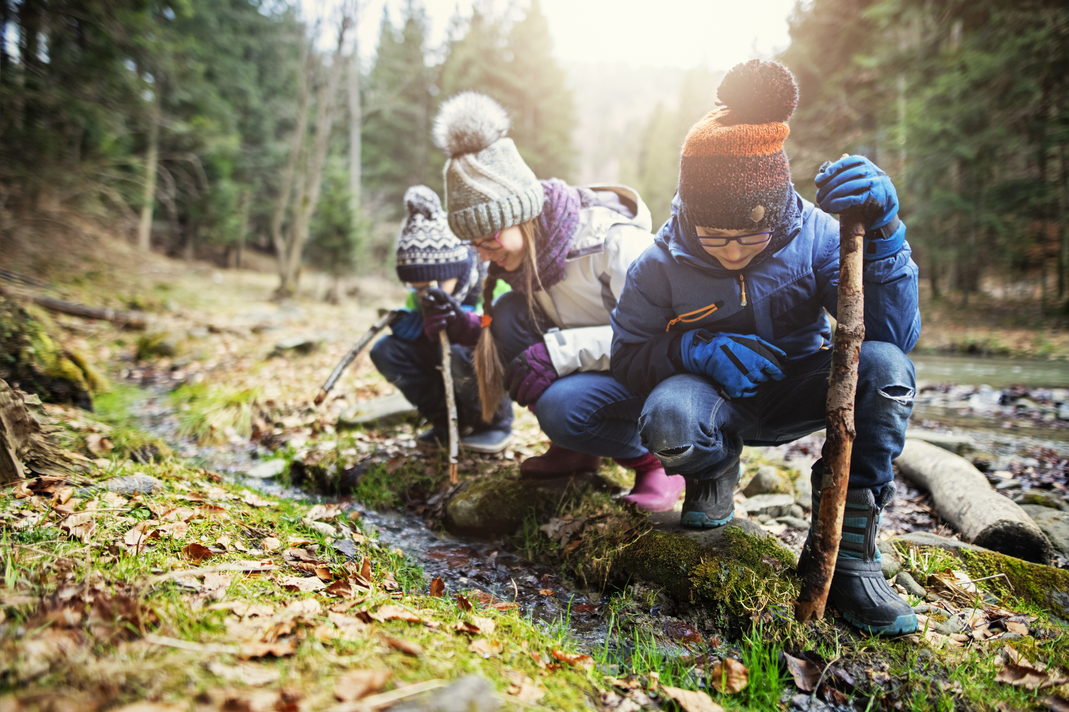 Happy kids hikers playing in stream with sticks