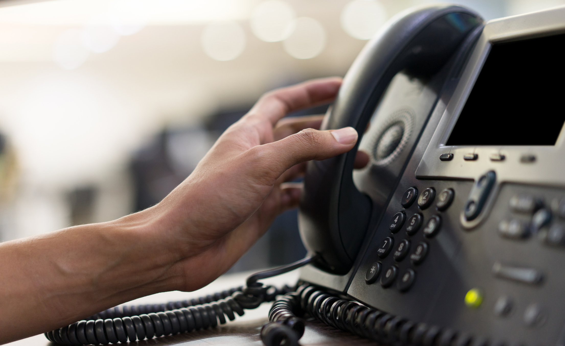 close up employee man hand touching handset of  telephone on desk for contact customer or receiving call , hotline  concept