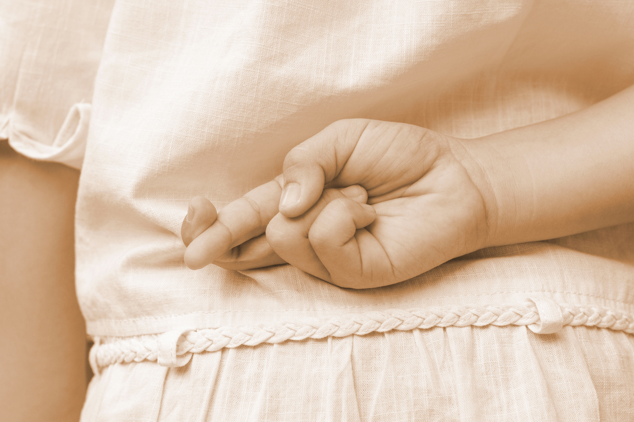 April Fools' Day.Close up of female kid hand crossing fingers behind her back. Girl child's Index finger and middle finger cross each other, lie and cheating concept in sepia vintage tone.