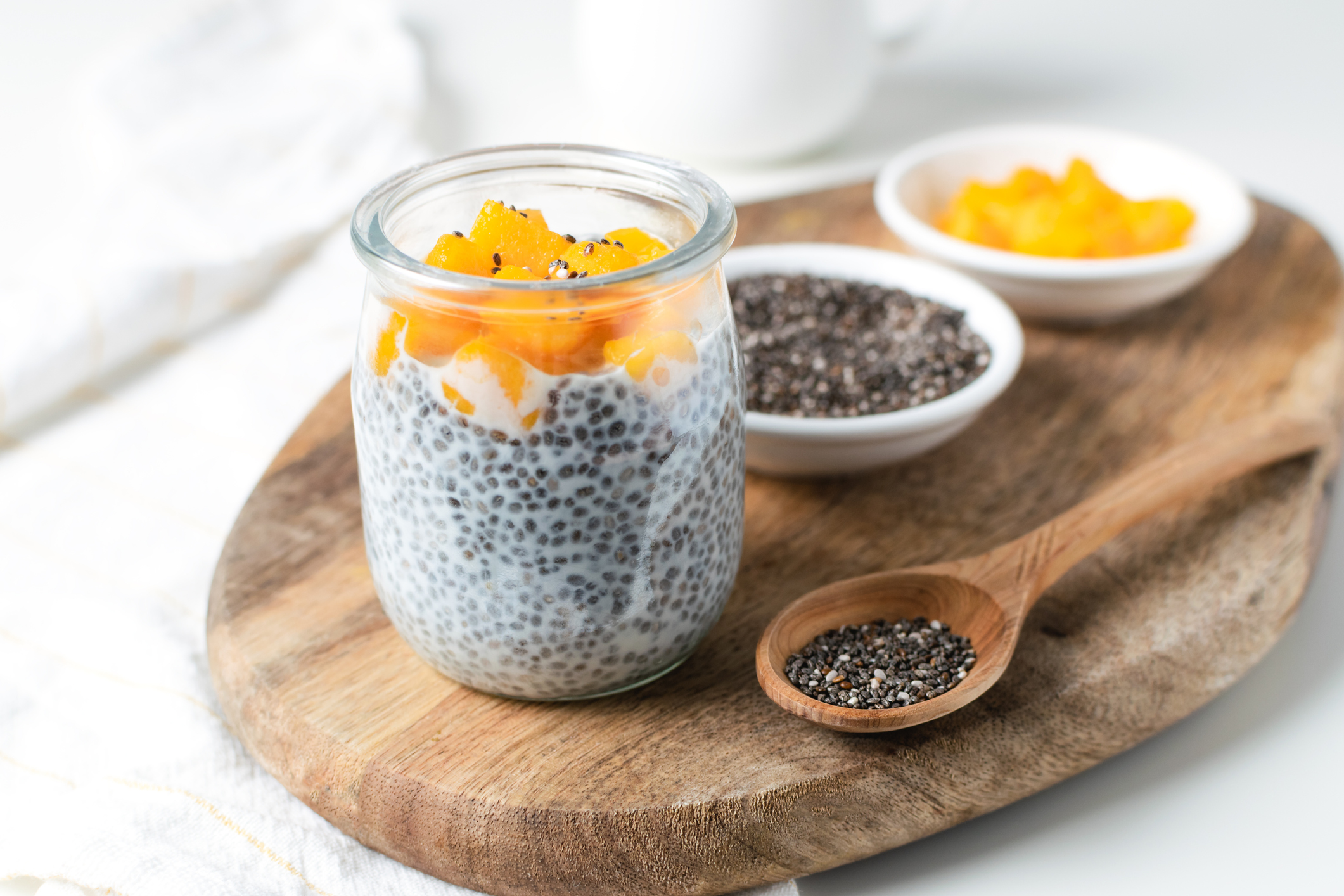 Chia pudding in glass jar with almond milk and mango on white background