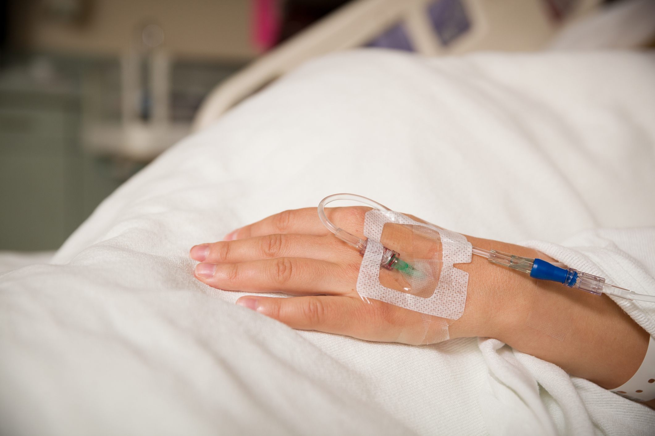 Close up hand of young patient with intravenous catheter for injection plug in hand during lying in the hospital bed.