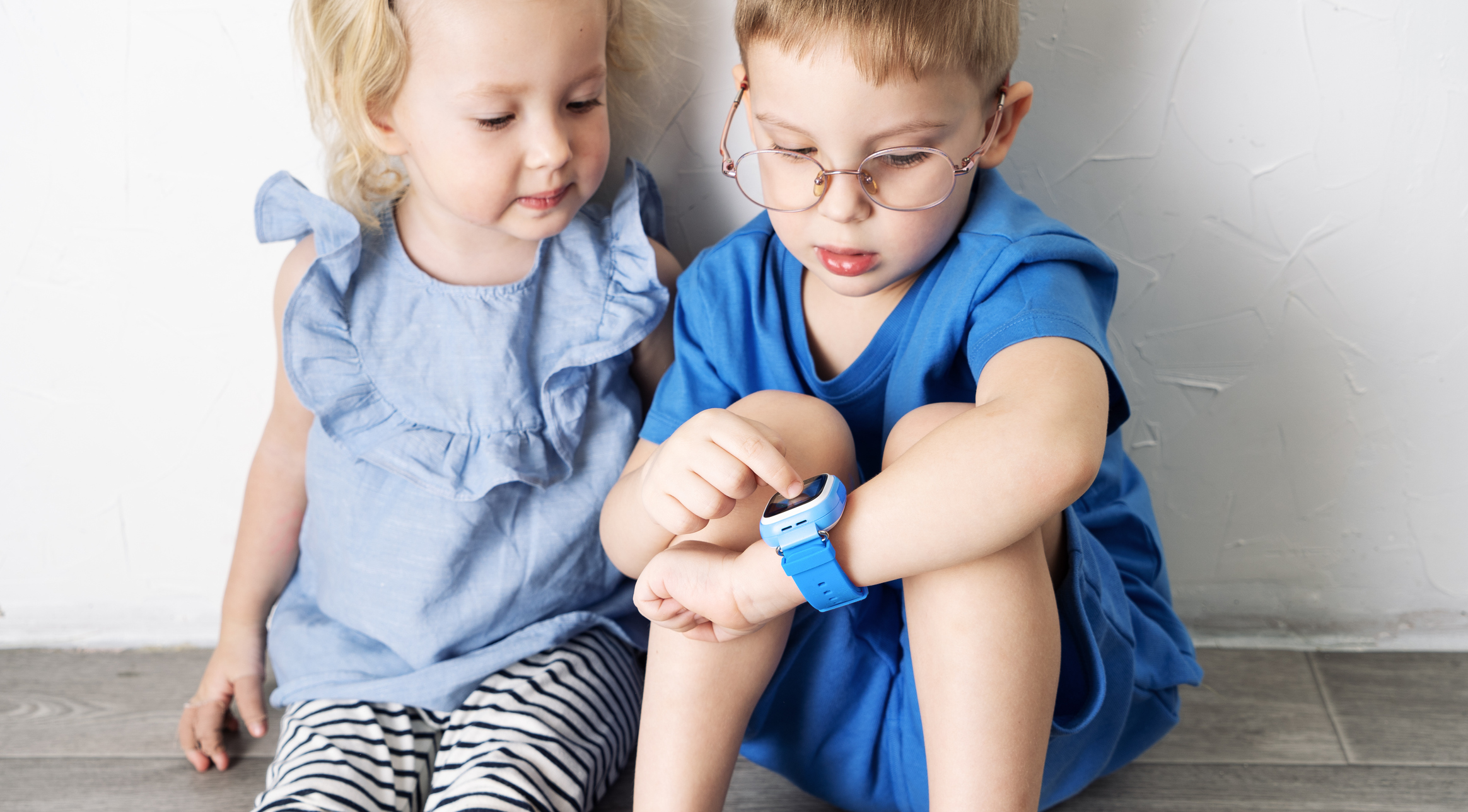 A little boy child in a blue T-shirt and glasses shows the girl his smart watch and presses a finger.