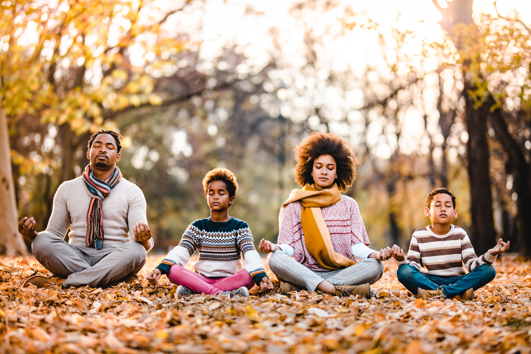 African American family doing Yoga relaxation exercises in autumn day.