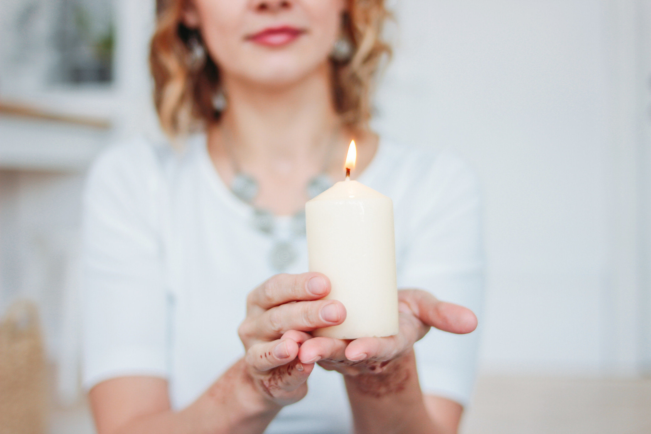 Blonde young woman in white clothing with mehendi holding burning candle