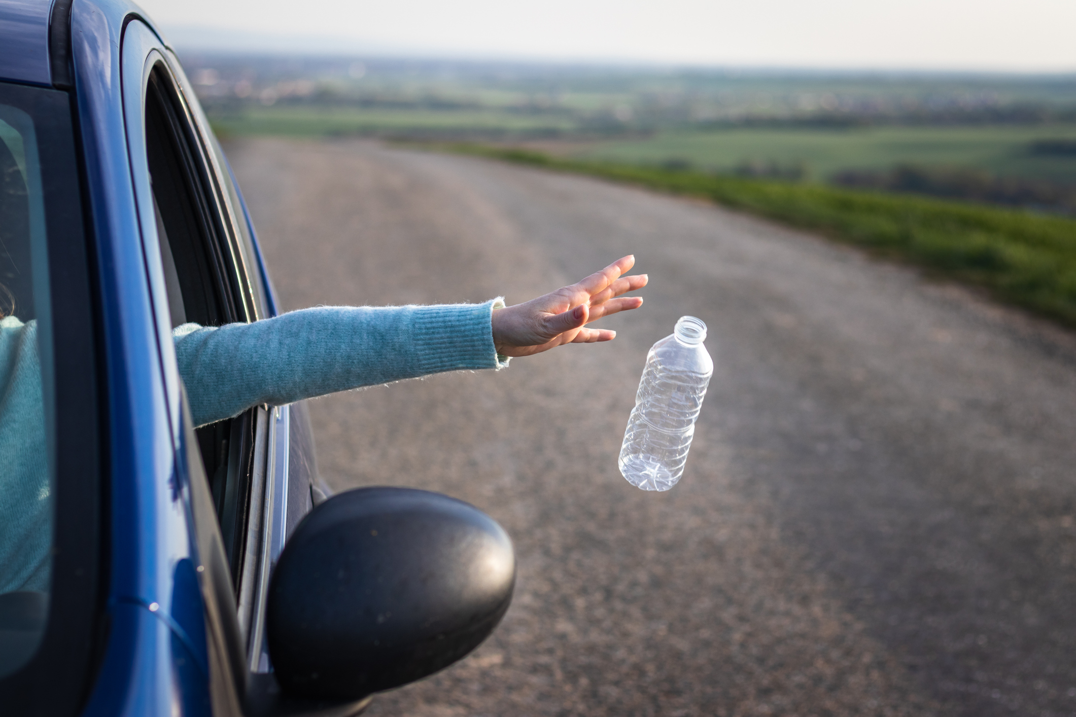 Do not pollute nature with plastic waste!  Driver throwing away plastic bottle from car window.