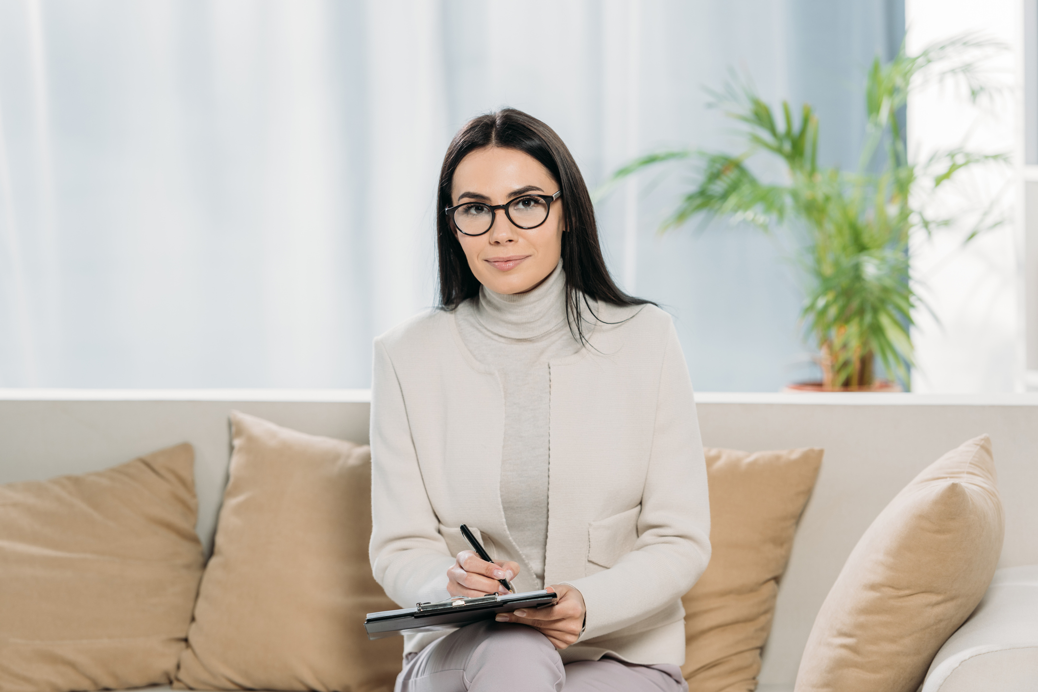 young female psychologist in eyeglasses writing on clipboard and smiling at camera