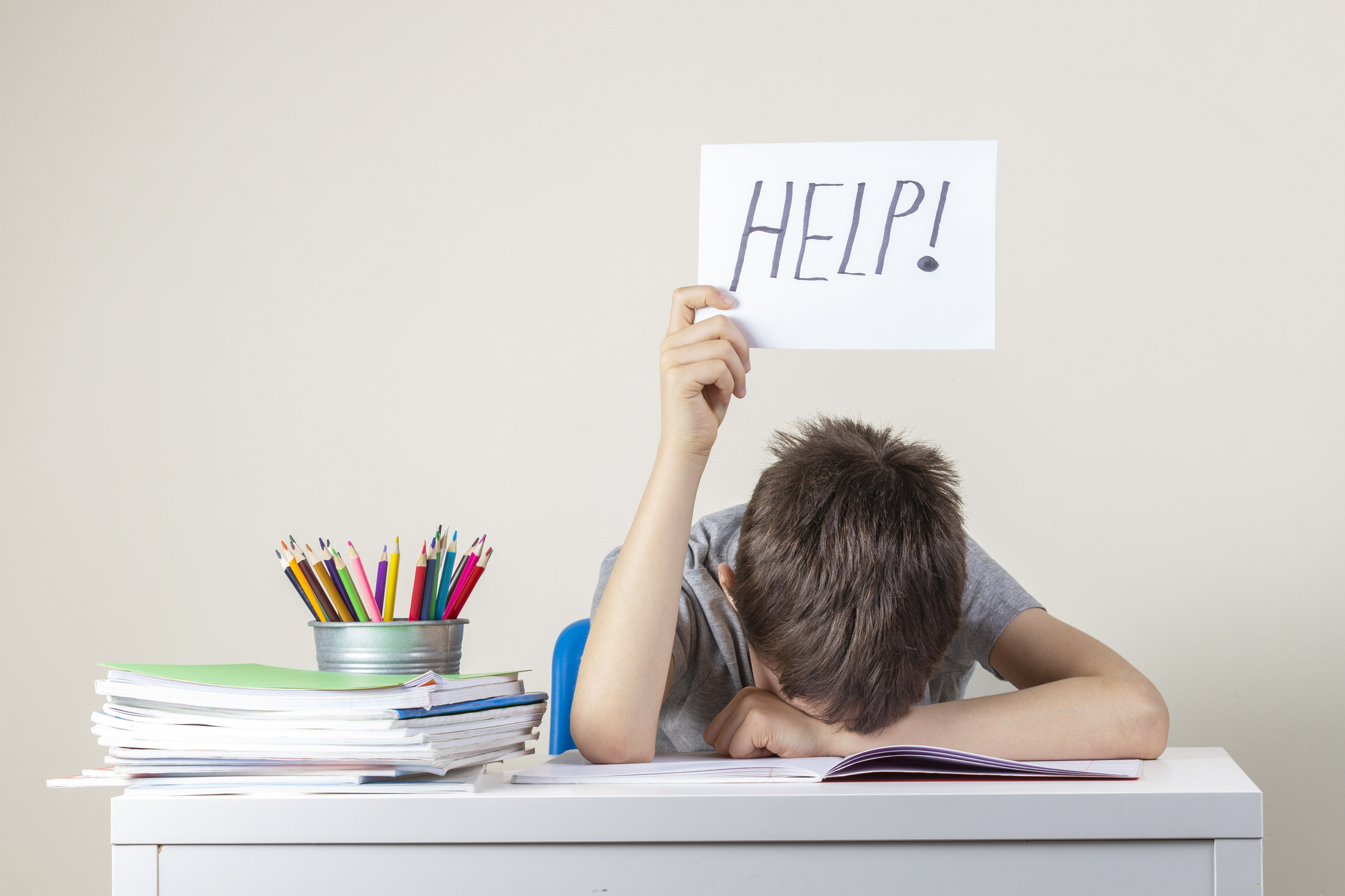 Sad tired frustrated boy sitting at the table with many books and holding paper with word Help. Learning difficulties, education concept.