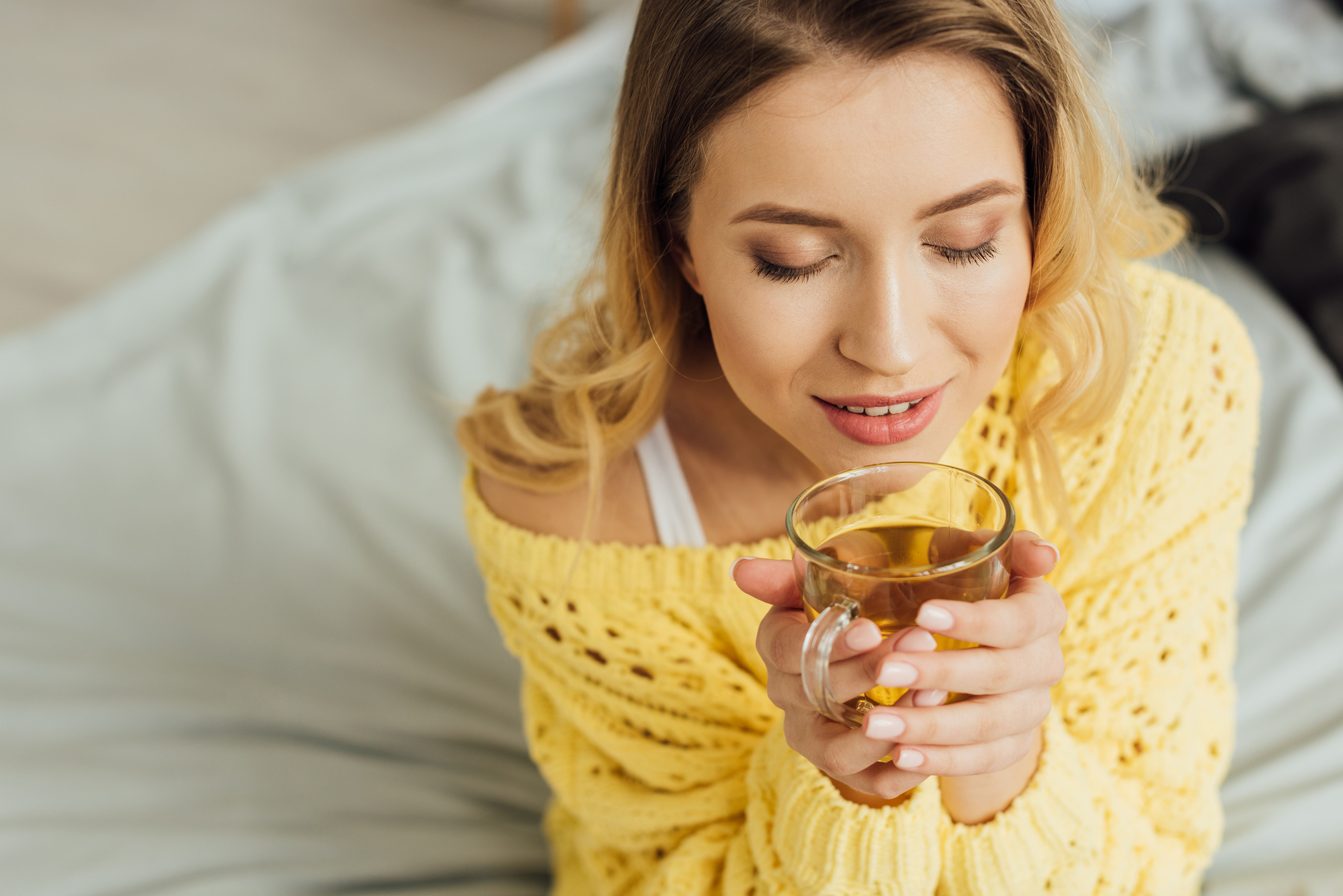 beautiful young woman with eyes closed holding cup of tea at home