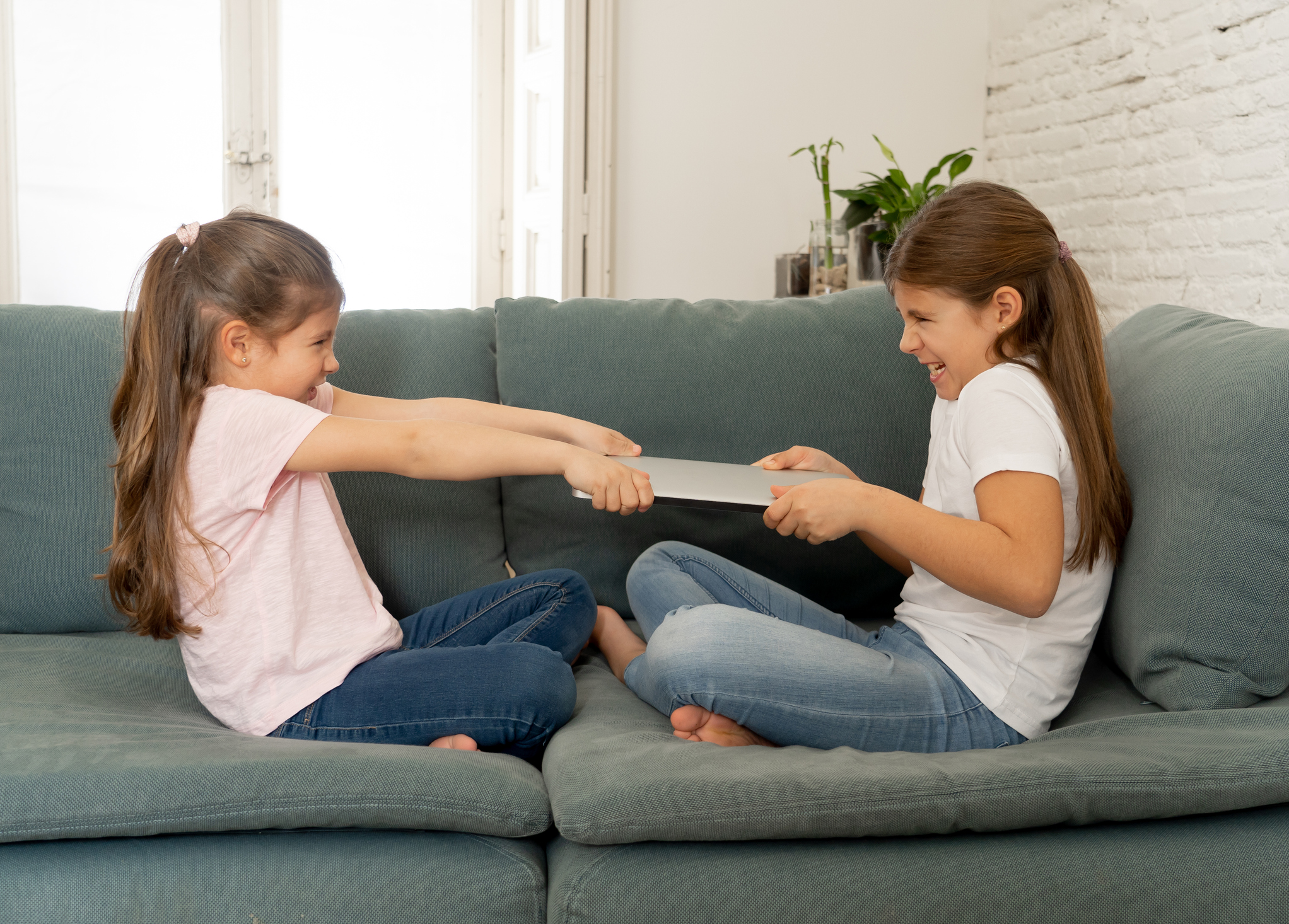 Younger and older girls fighting for laptop arguing over playing on the internet. Lifestyle portrait of sisters not sharing computer in Relationship between siblings and technology addiction concept.