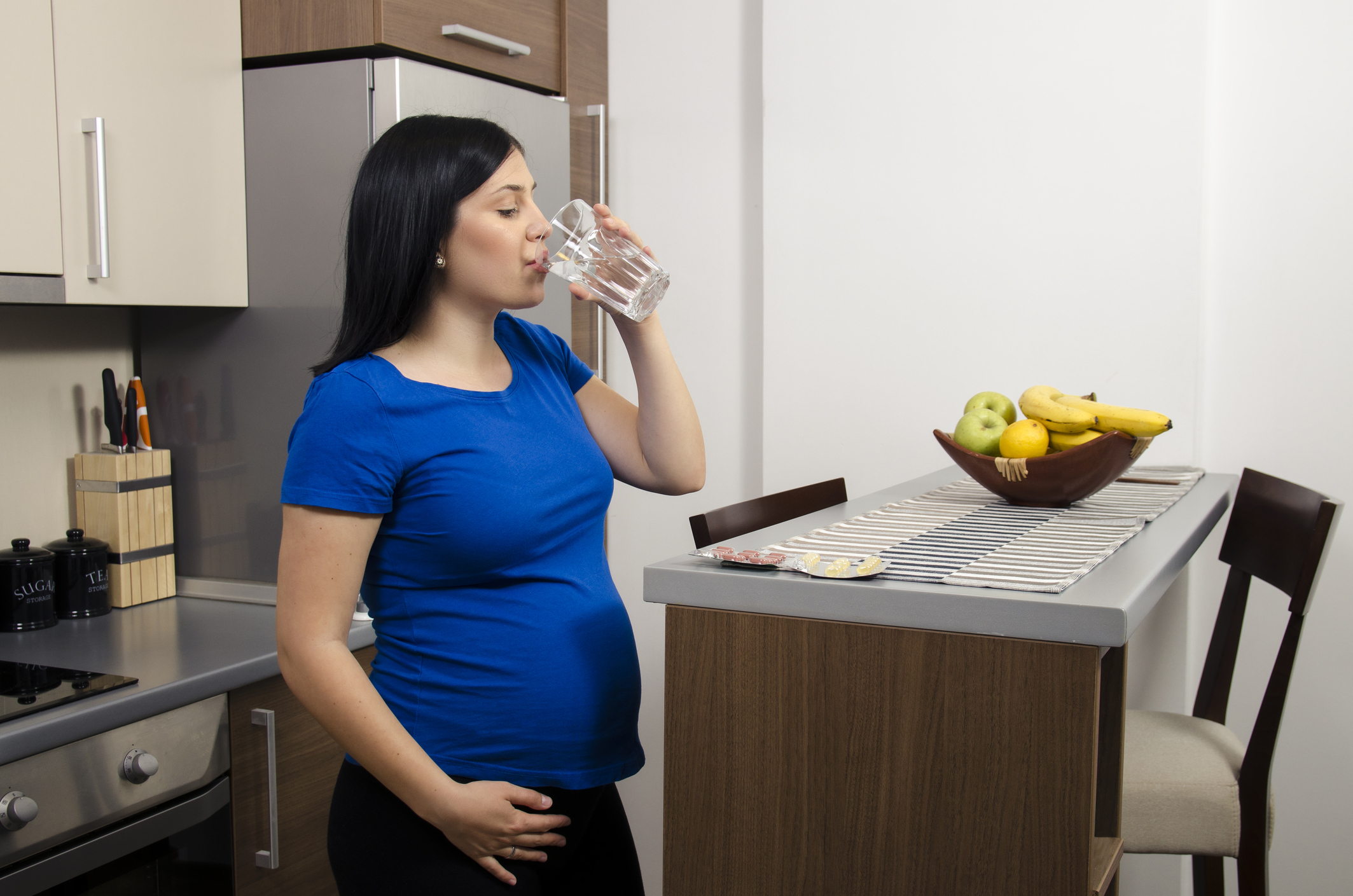 Young pregnant woman drinks water in kitchen