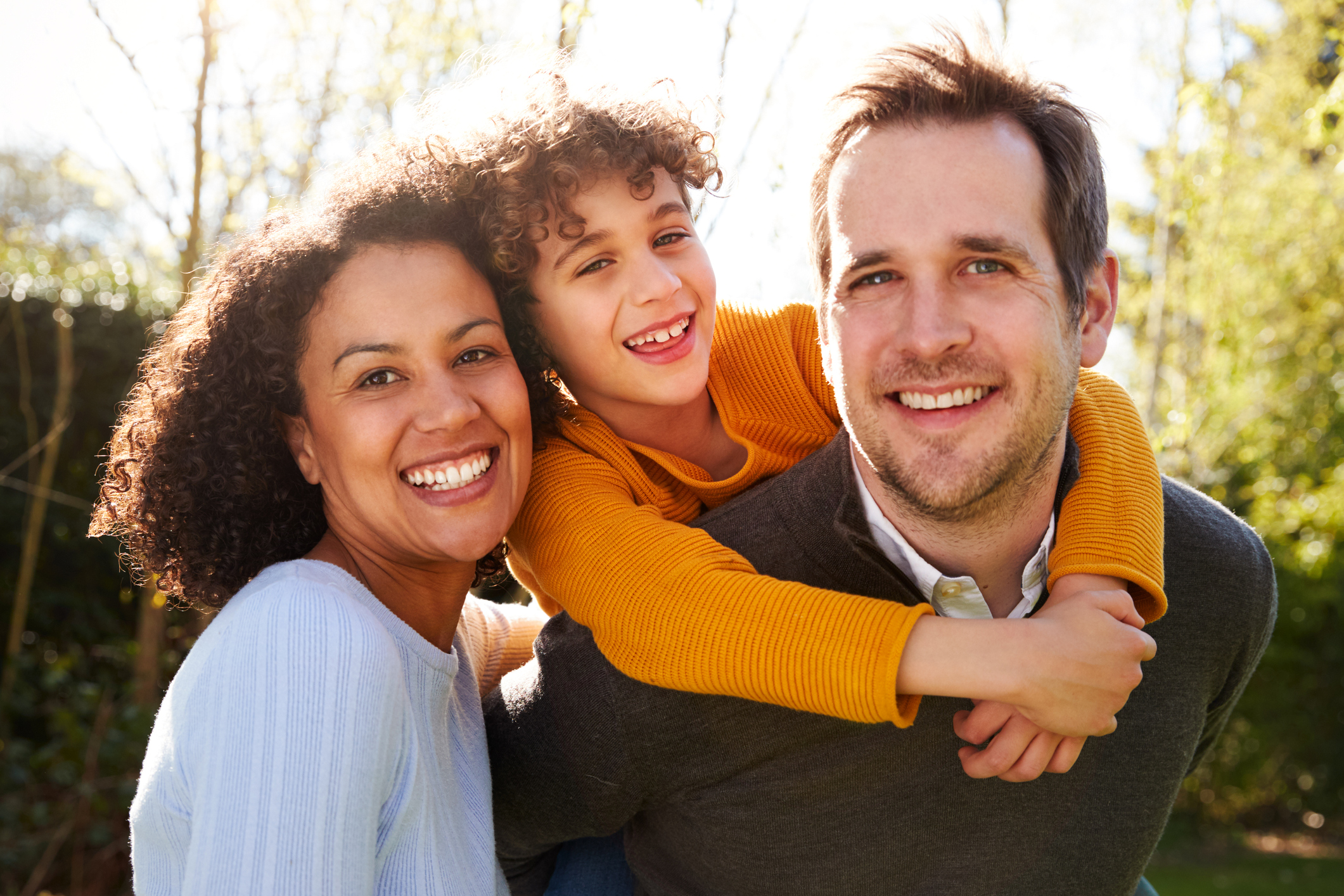 Outdoor Portrait Of Smiling Family In Garden At Home Against Flaring Sun