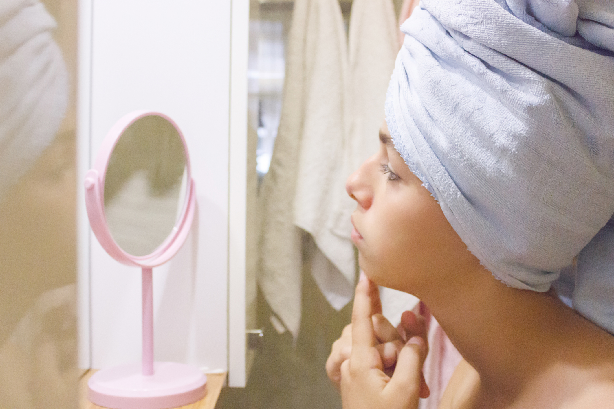 Young beautiful teen girl in a towel squeezes a pimple acne in front of a mirror