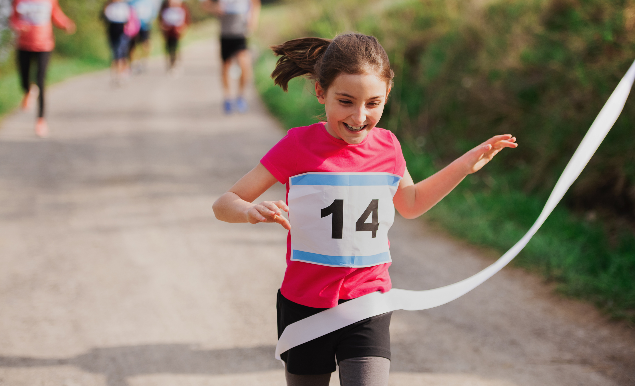 Small girl runner crossing finish line in a race competition in nature.