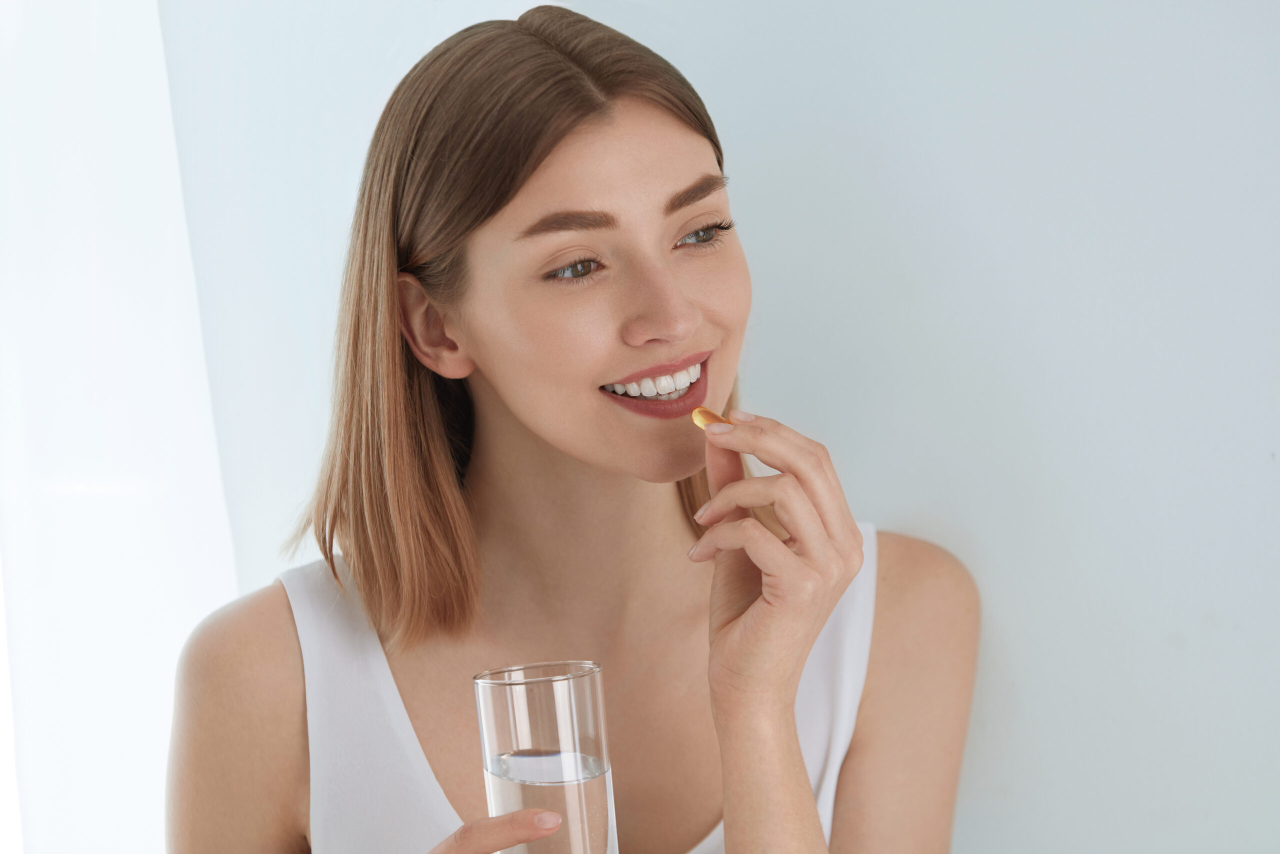 Woman taking vitamin pill with glass of fresh water indoors