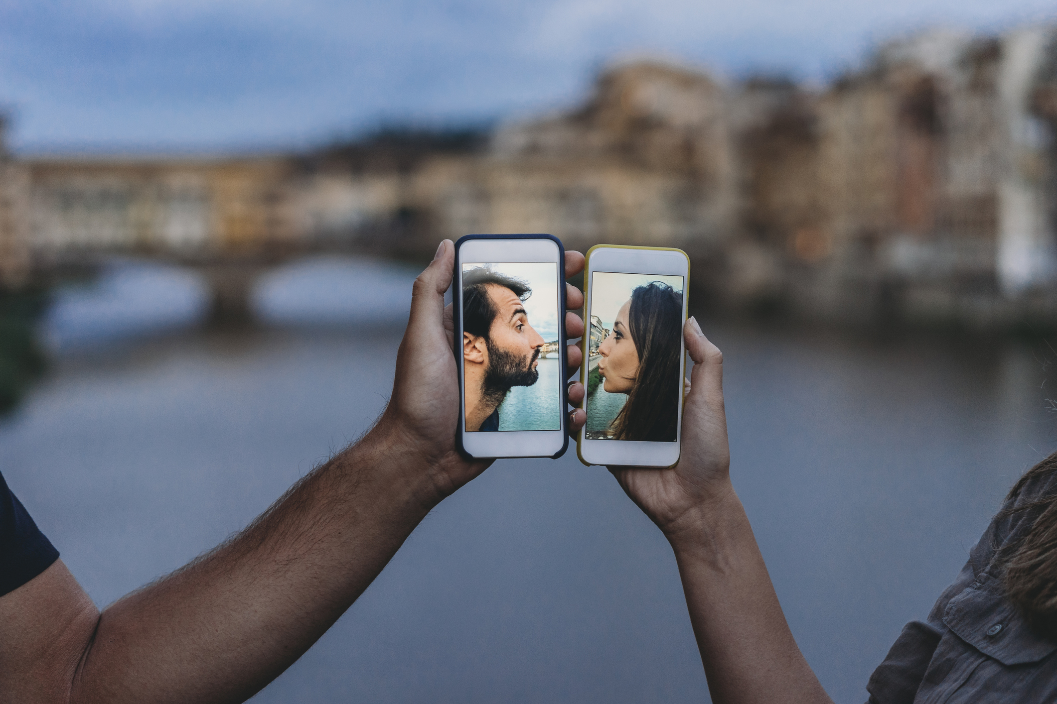 Conceptual shot of a young adult couple kissing via mobile phone