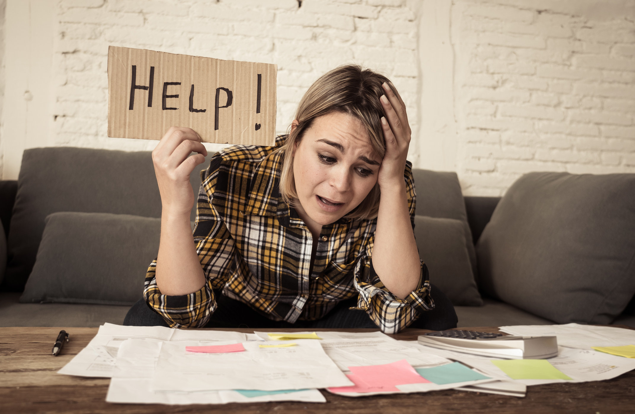 Lifestyle portrait of worried desperate young woman feeling stressed while working through finances at home showing Help sign. In single mother paying off debts and bills and financial problems.