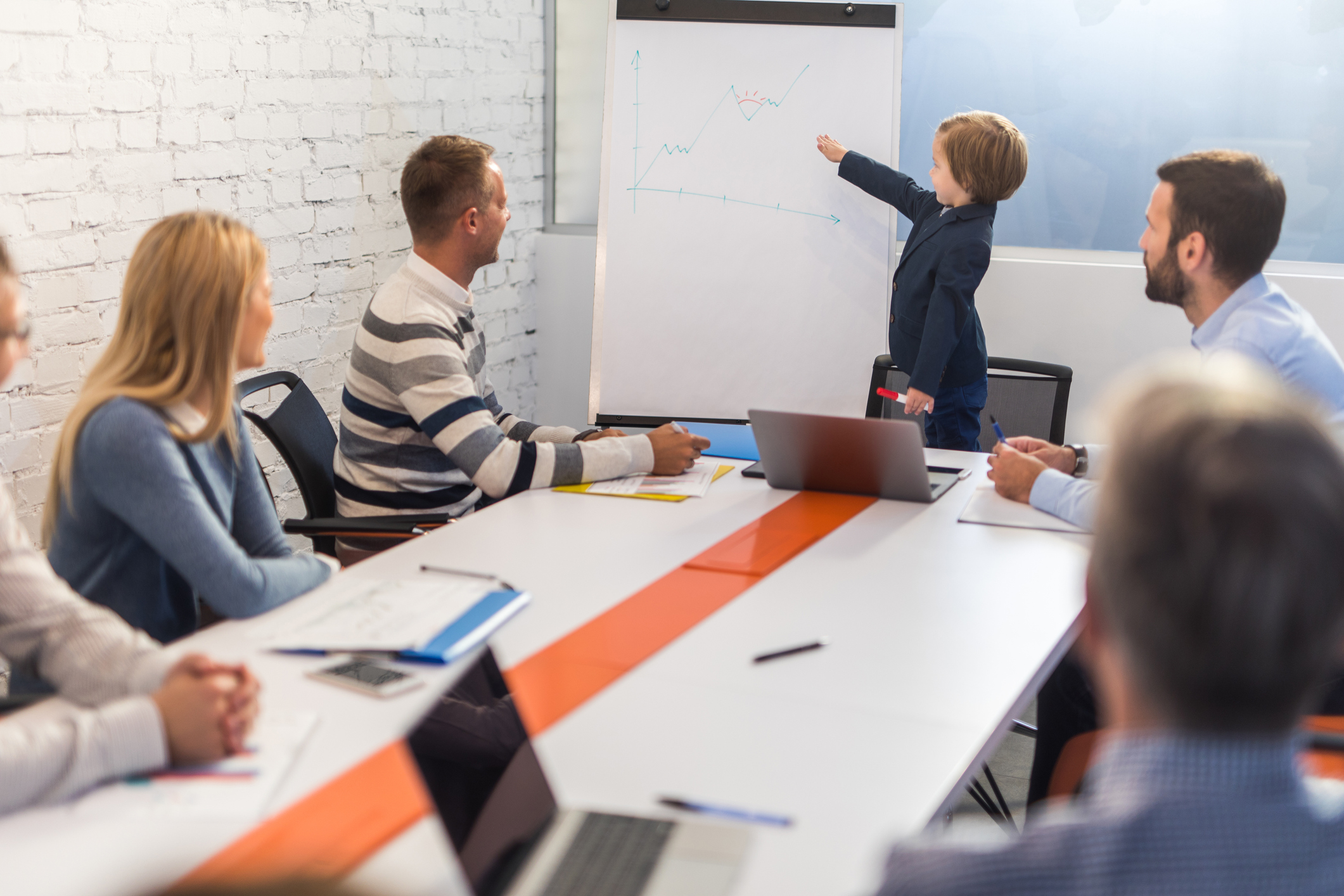 Little business boy holding a presentation to group of adults in board room.