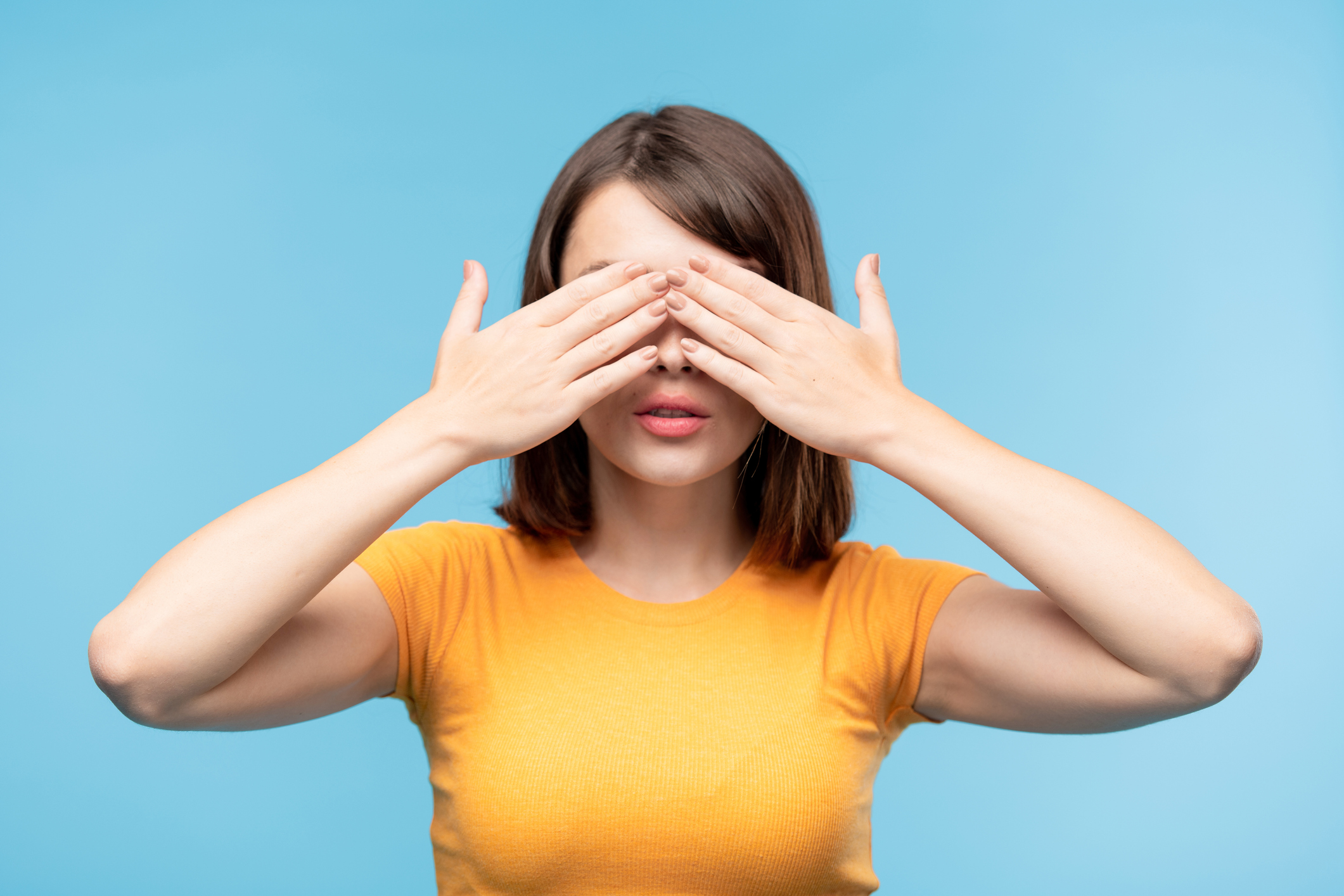 Young brunette female in yellow t-shirt covering her eyes with hands