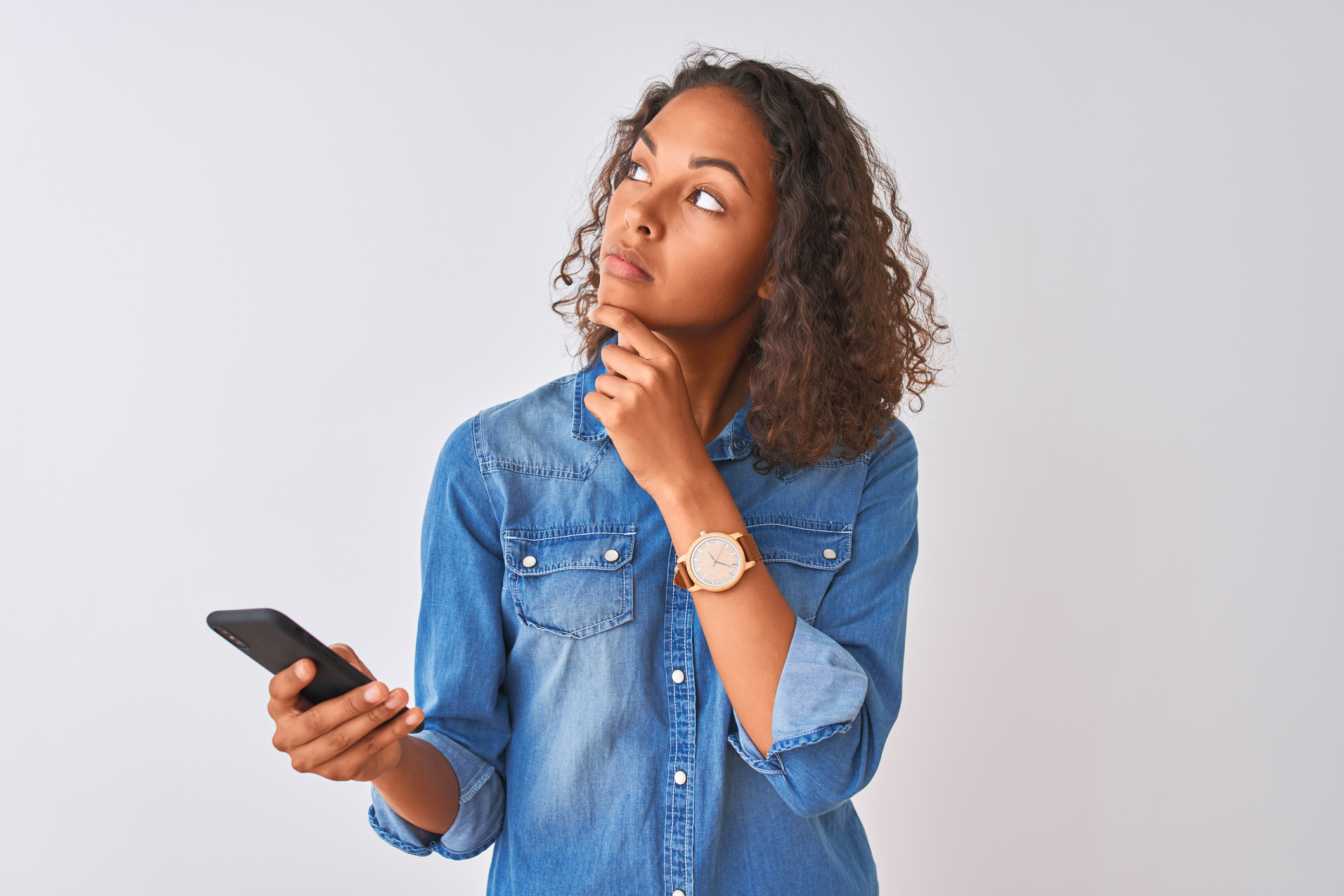 Young brazilian woman using smartphone standing over isolated white background serious face thinking about question, very confused idea