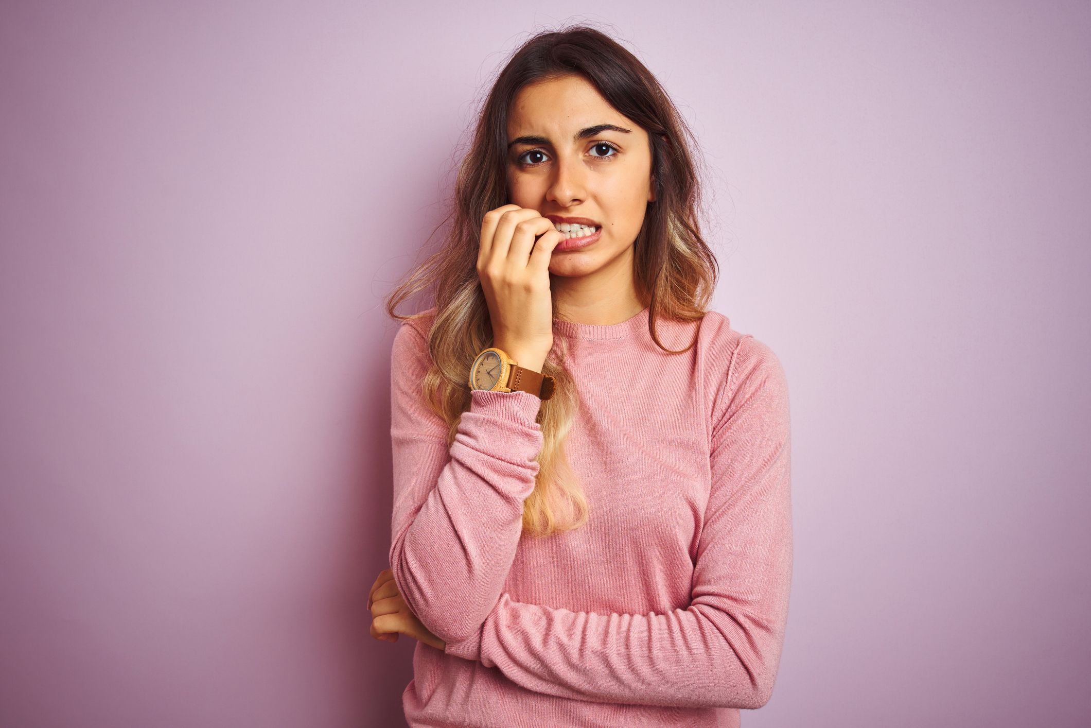 Young beautiful woman wearing a sweater over pink isolated background looking stressed and nervous with hands on mouth biting nails. Anxiety problem.