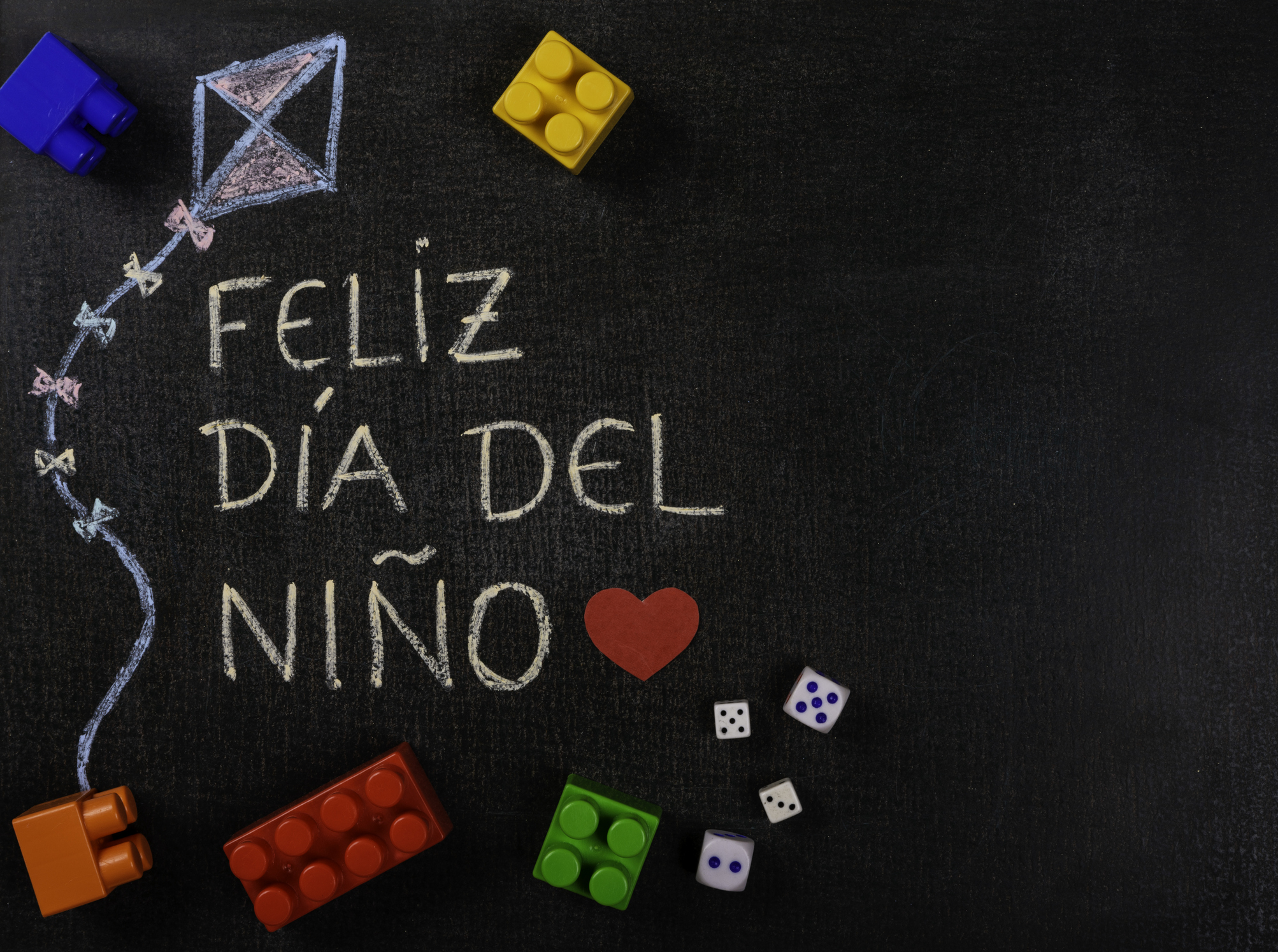 Blackboard written feliz dia del niño (spanish). Kite design with assembling pieces and game dice. Copy space"n