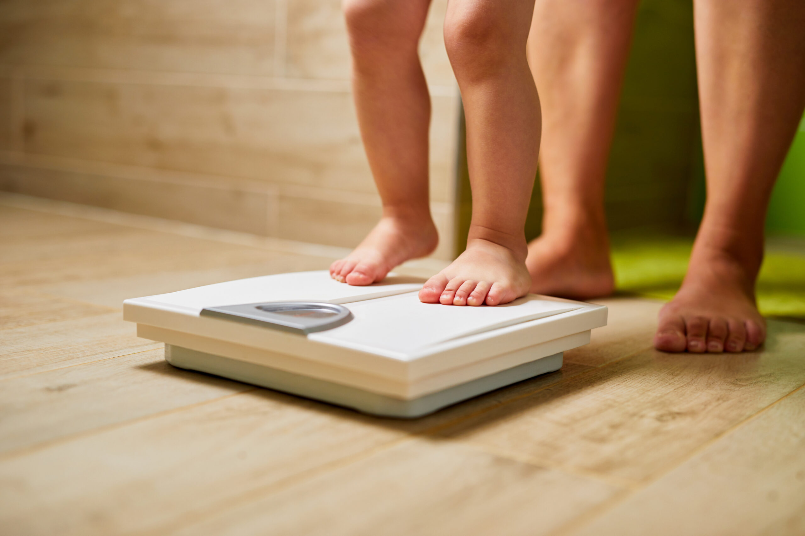 Little child standing on scale weight with his mother