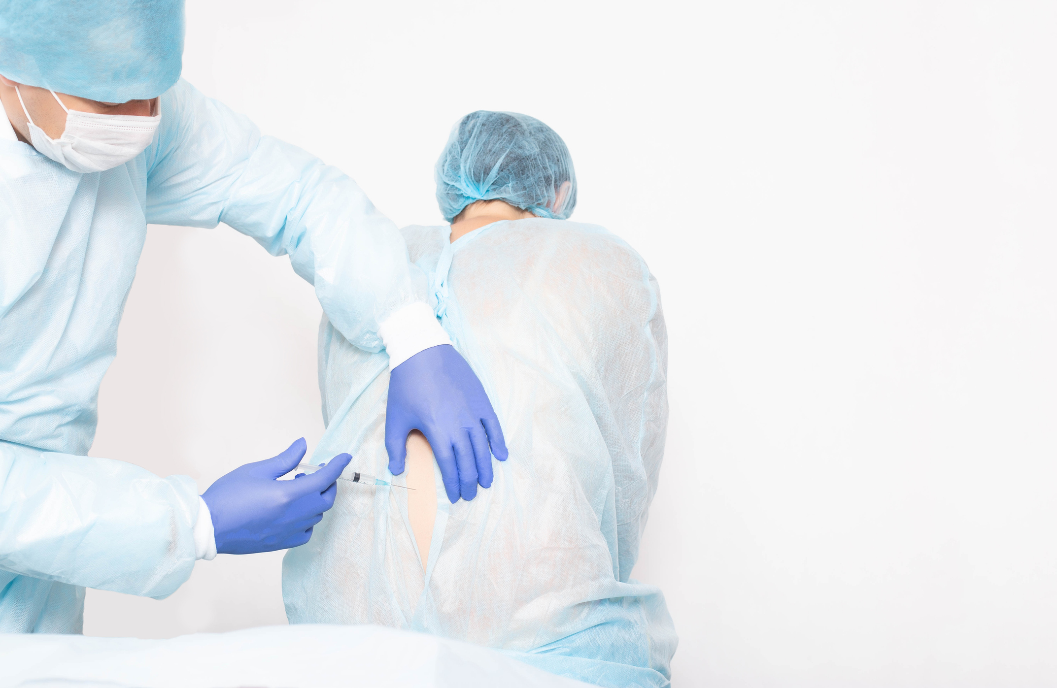 A male anesthesiologist performs a surgical procedure that introduces epidural anesthesia into the back of a girl during childbirth, medic, copy space