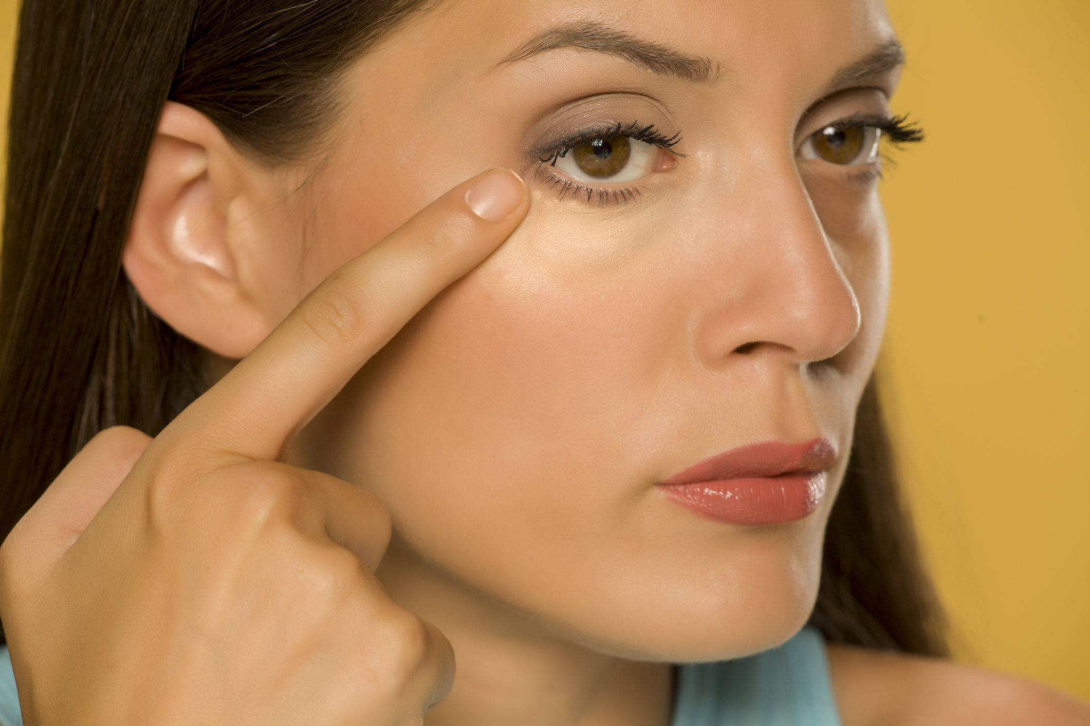 Young woman touching her low eyelids on yellow background