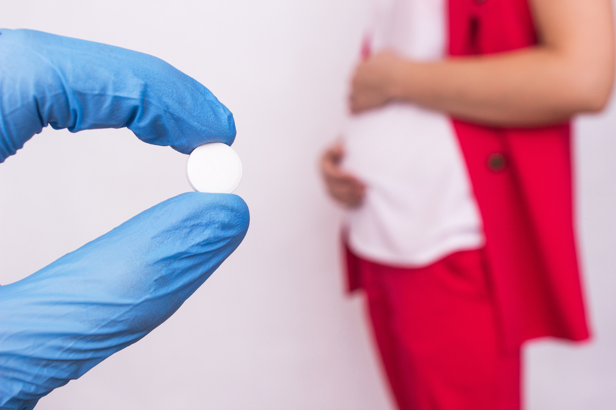 The doctor holds a pill in the form of a complex of vitamins and folic acid on the background of a pregnant girl, lack of vitamins and calcium during pregnancy