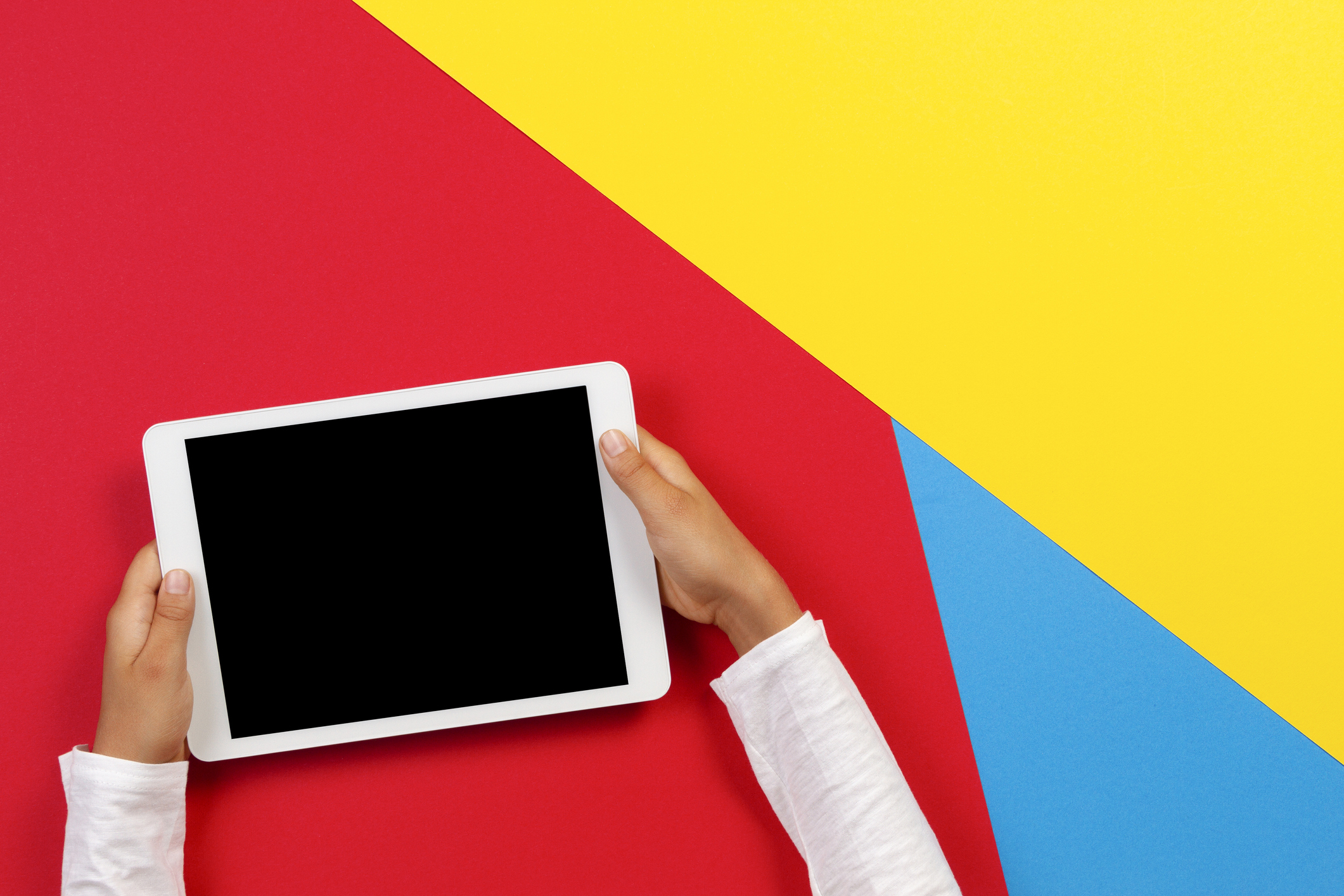 Kid hands with tablet computer on red, yellow and blue background