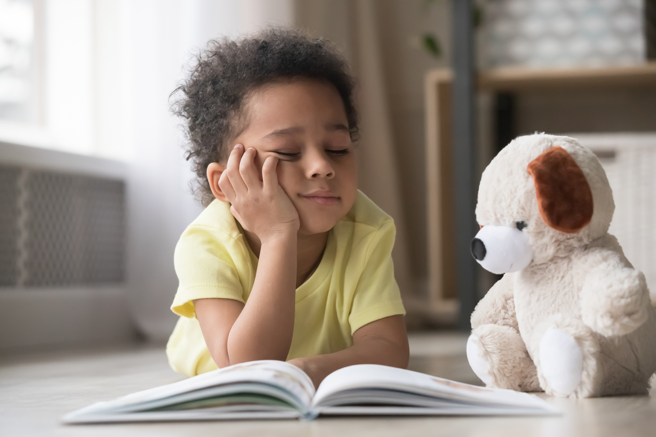 Bored little boy reading book lying on floor