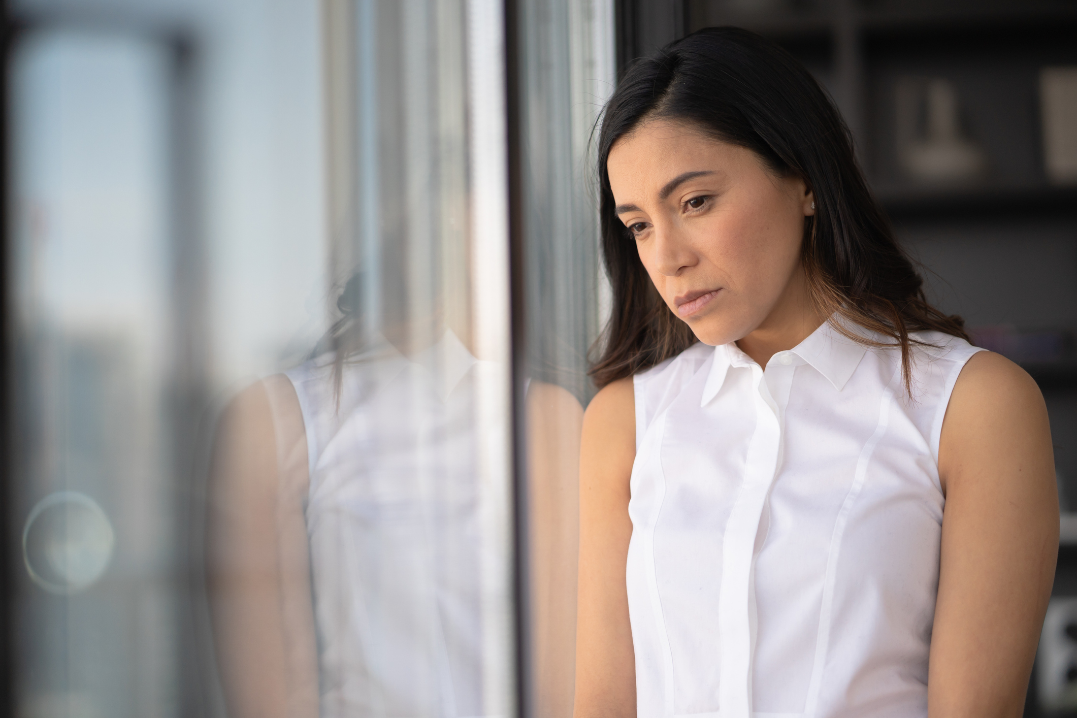 Sad Latina woman leaning on window