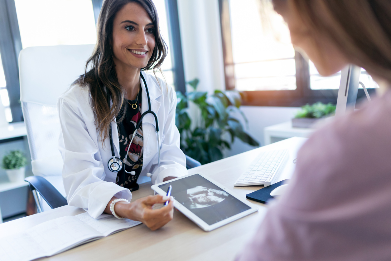 Pretty young woman gynecologist using digital tablet for showing the ultrasound to her pregnant patient in the clinic.